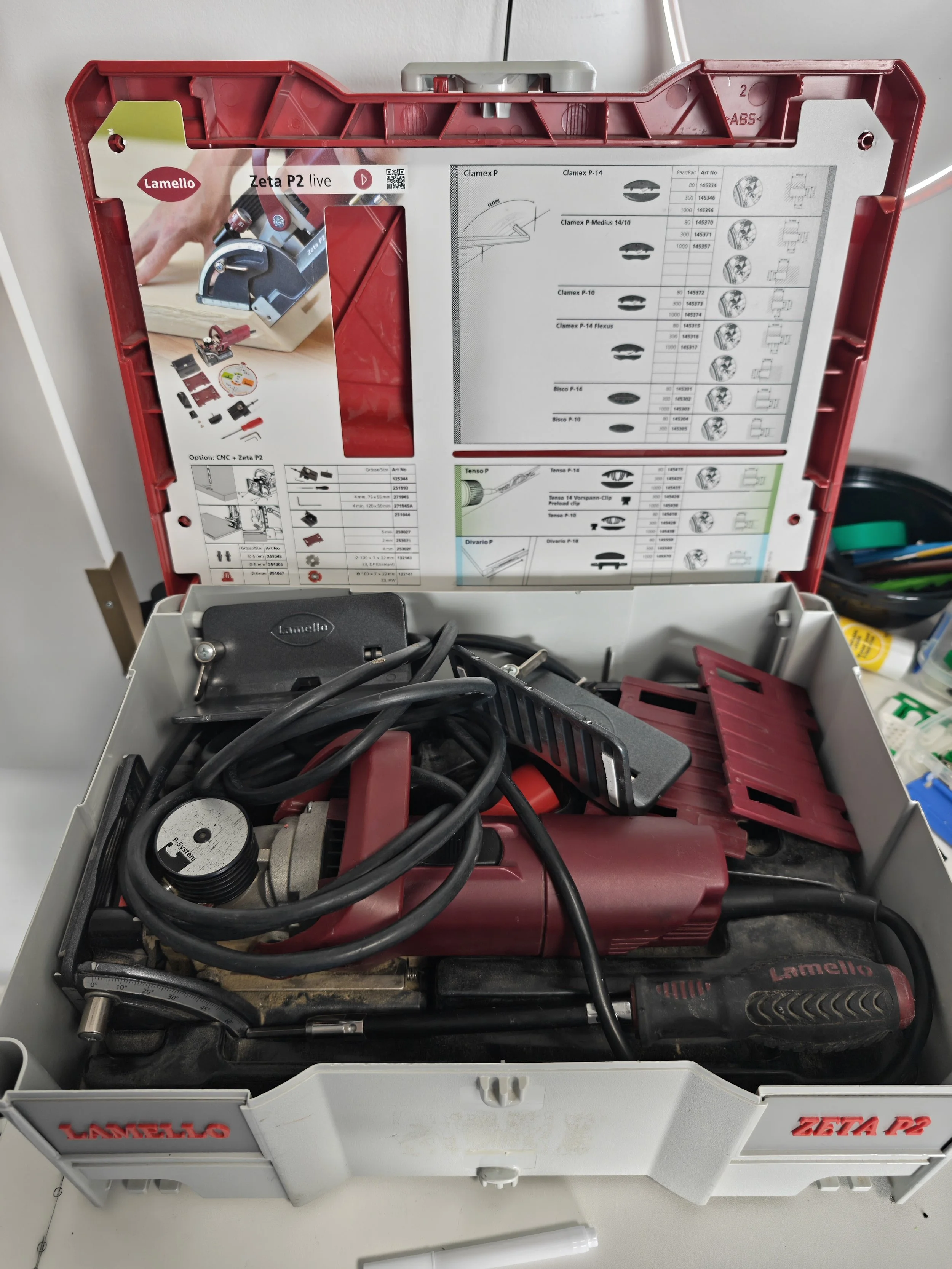 Open red toolbox containing various power tools and accessories, including a Lamello Zeta P2 live biscuit joiner, cables, and a level.