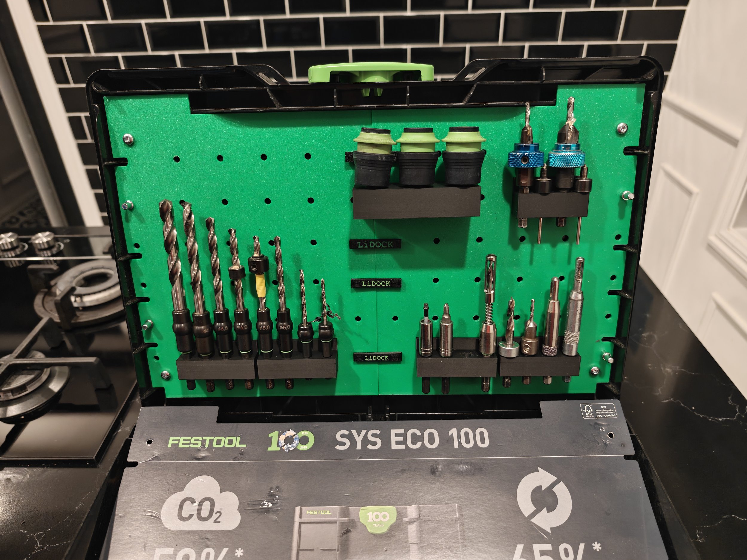 A green and black toolbox containing various drill bits, adapters, and tools, with a Festool SYS ECO 100 label on it.