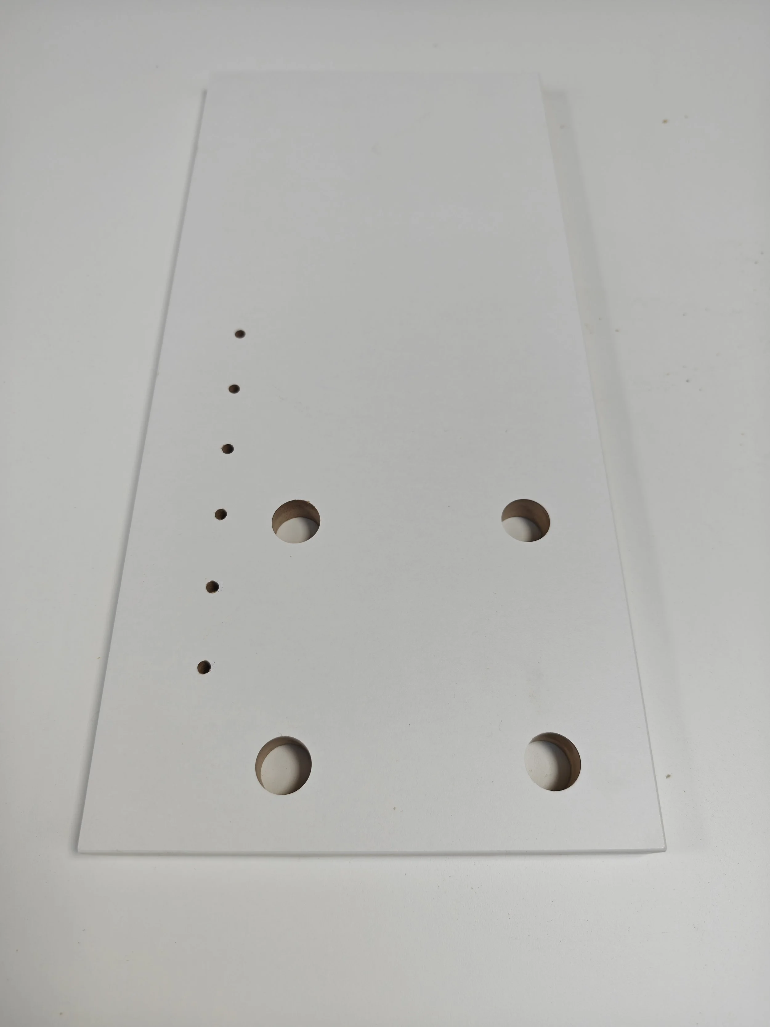A white rectangular piece of material with evenly spaced holes of varying sizes, placed on a white surface.