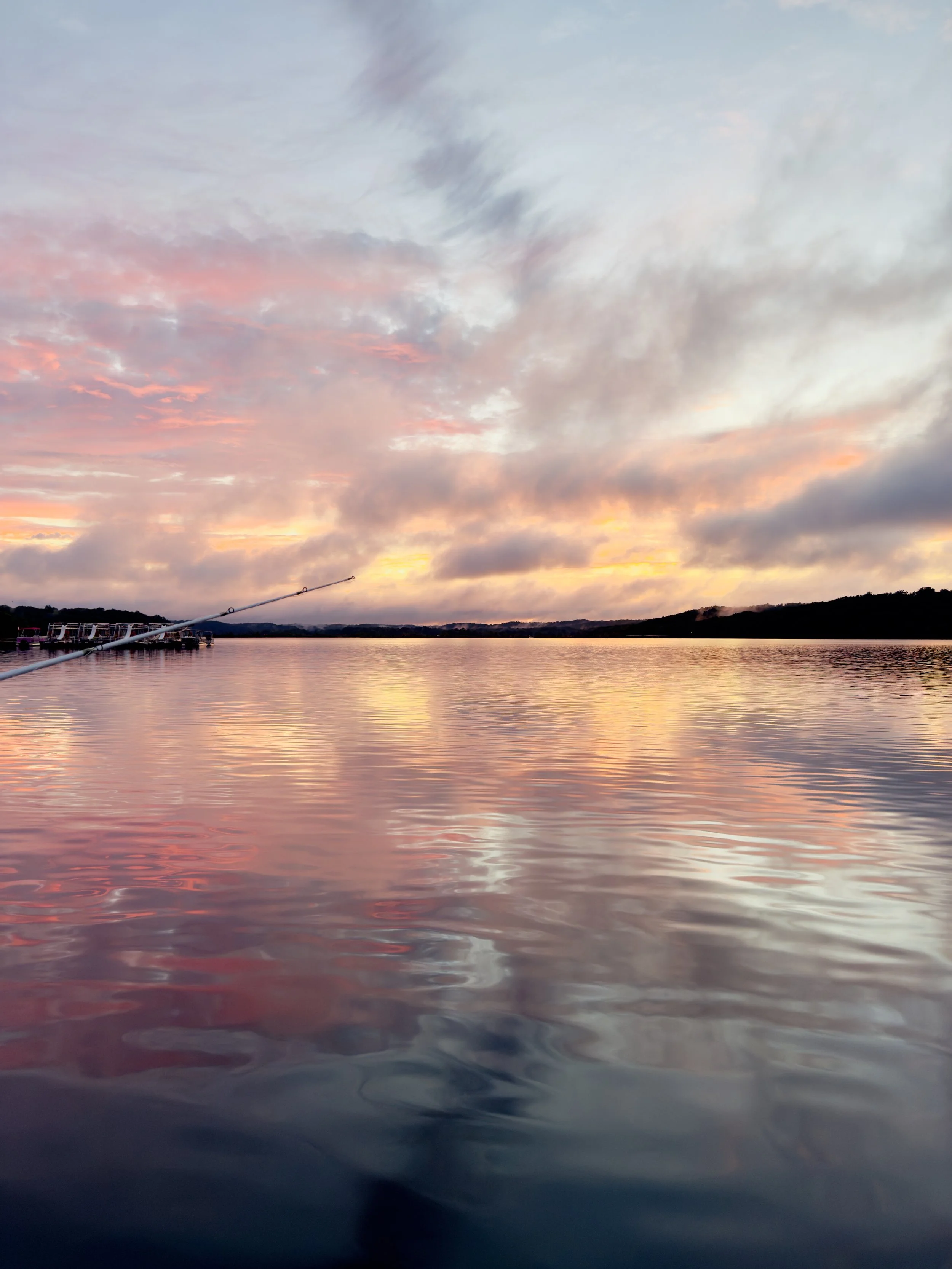A tranquil body of water at sunset with colorful clouds in the sky and a boat dock on the left side.