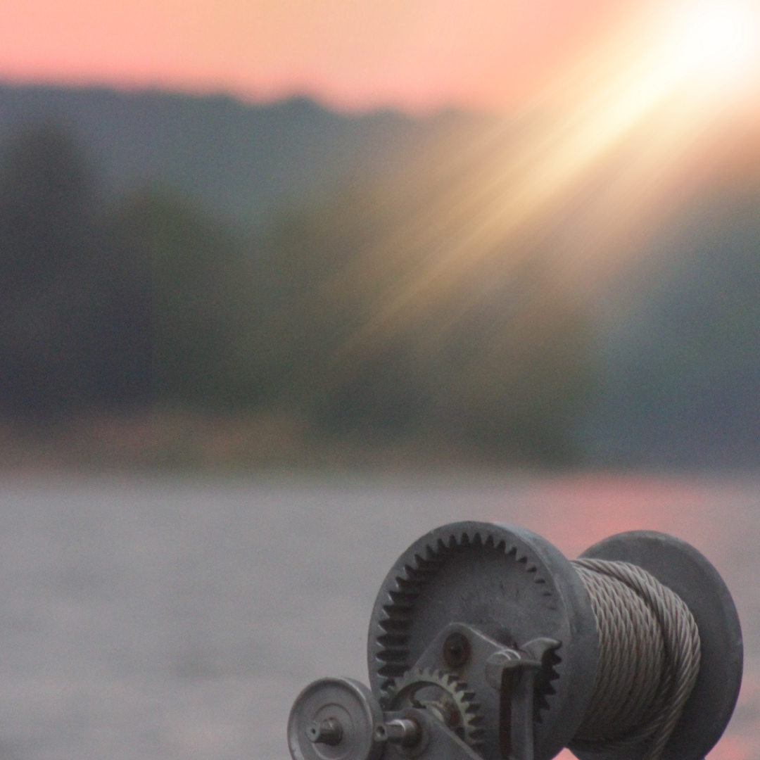 Close-up of a spool of thick rope or cable resting on a surface with a blurred natural landscape and sunset in the background