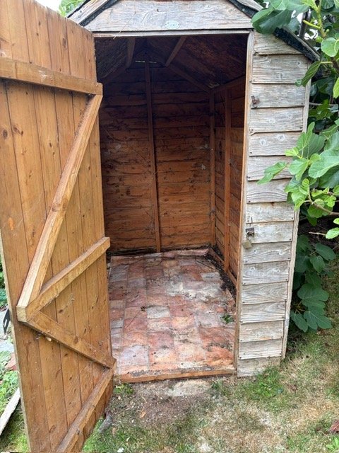 Empty wooden shed with an open door, brick floor, and outside greenery