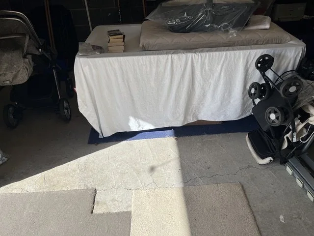 Table covered with a white cloth, with a mattress and some items on top, next to a golf putter display rack and a gray stroller.