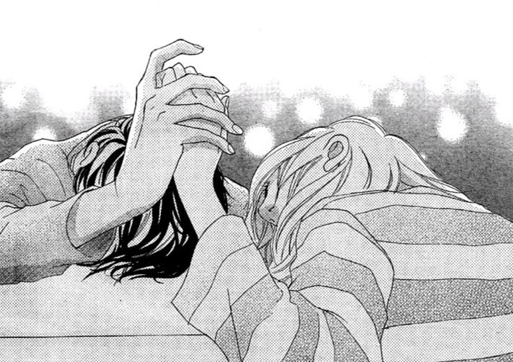 Two people lying down, holding hands and resting their heads on each other's shoulders, with blurred lights in the background.