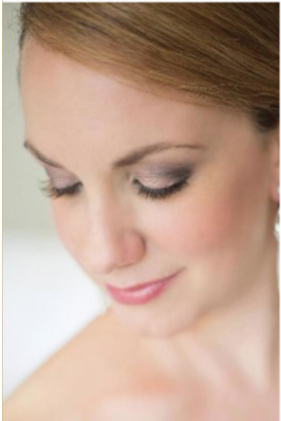 Close-up of a woman with makeup looking down with a soft smile.