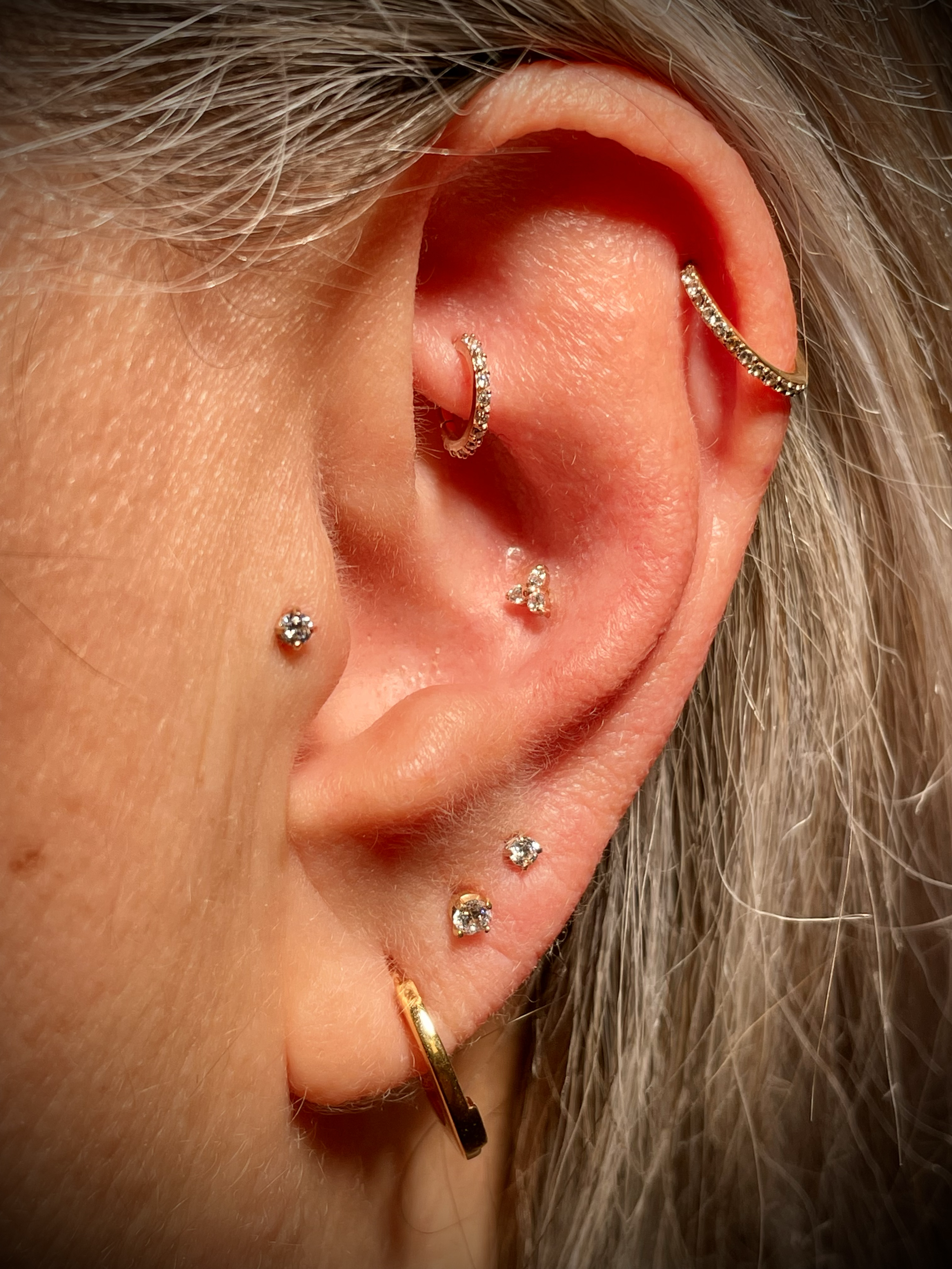 Nahaufnahme eines Ohrs mit mehreren kleinen, funkelnden Ohrringen aus Gold und Diamanten.