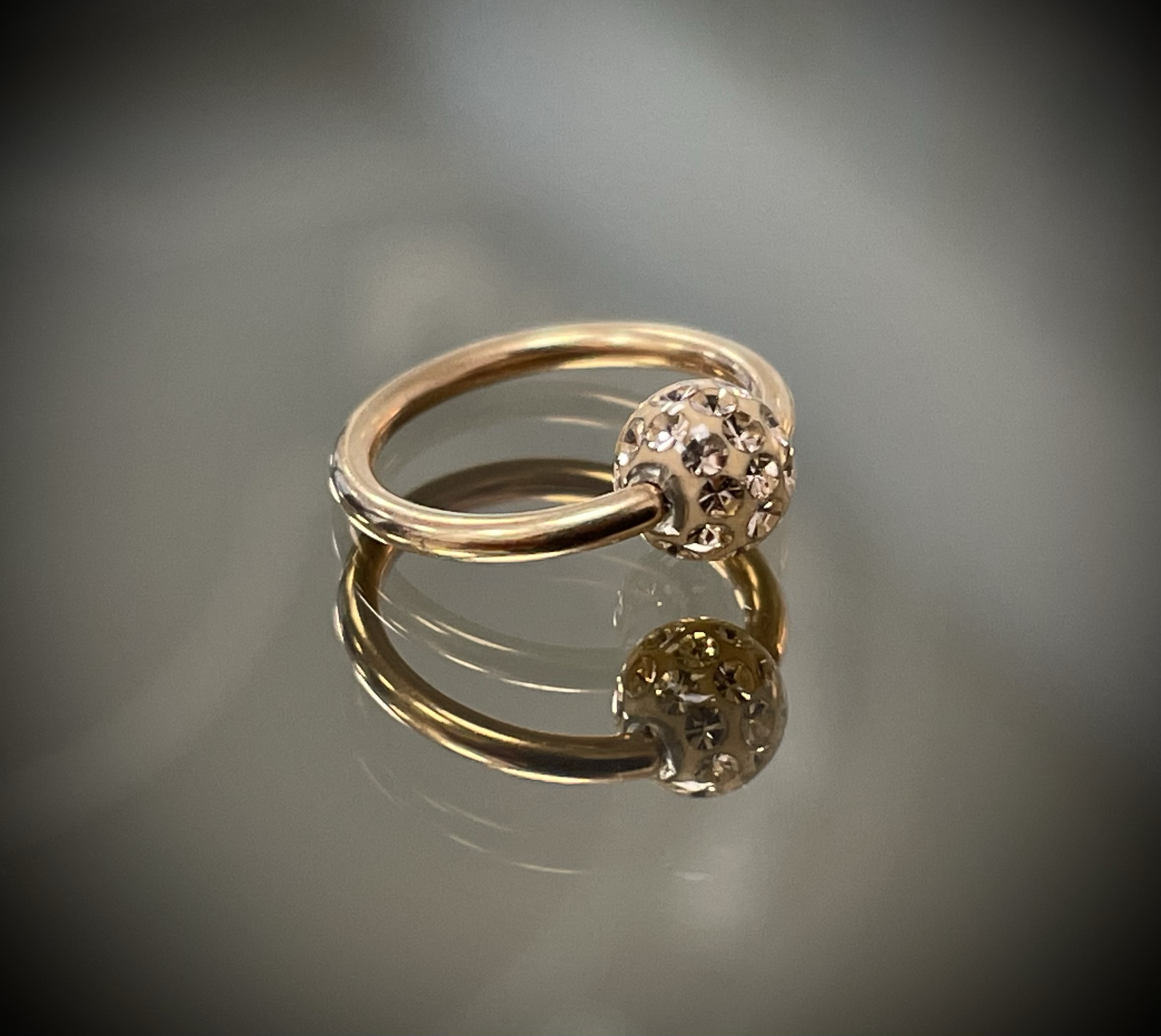 Goldenes Schmuckstück mit zahlreichen kleinen funkelnden Steinen, vermutlich ein Ring, auf einer spiegelnden Oberfläche