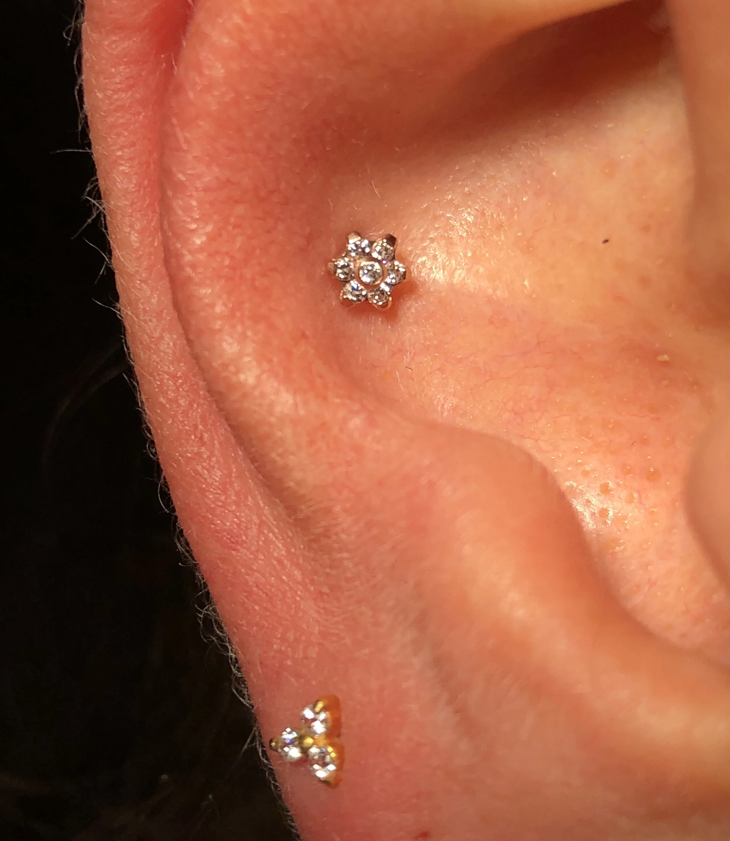 Nahaufnahme eines menschlichen Ohrs mit einem dekorativen Piercing, das eine kleine Blume mit Glitzersteinen darstellt.