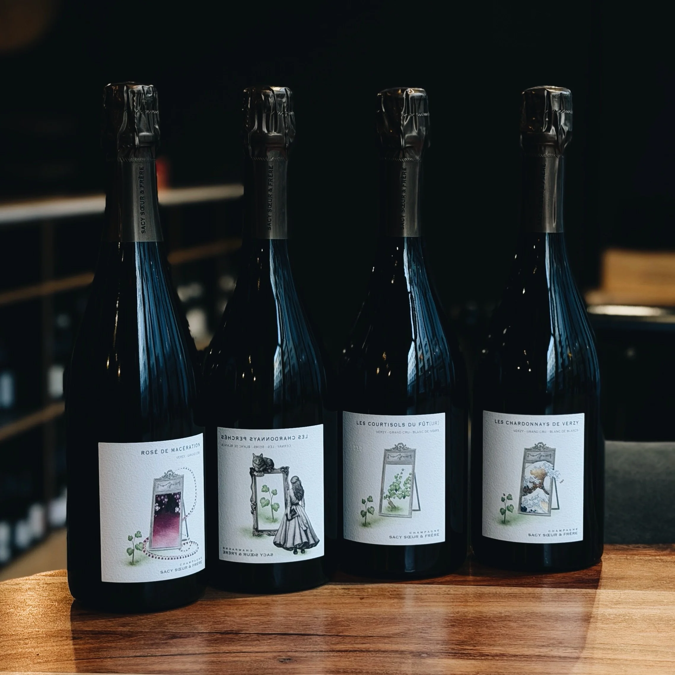 Quatre bouteilles de champagne alignées sur une surface en bois, avec des étiquettes illustrant des cartons de plantes et d'animaux, et le texte en français.