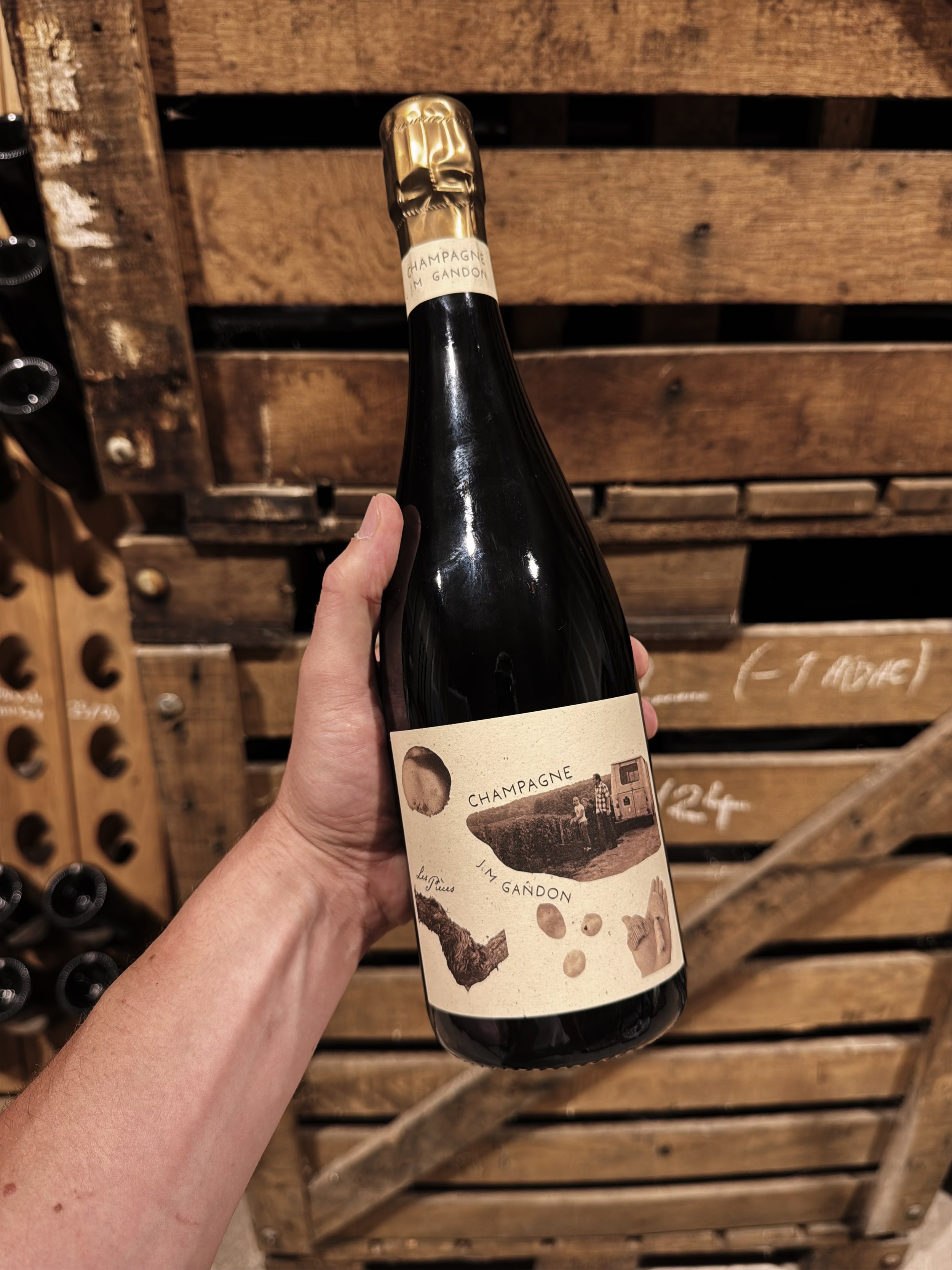 Bouteille de champagne noir avec étiquette vintage, tenu par une personne devant un mur en bois de cagib.