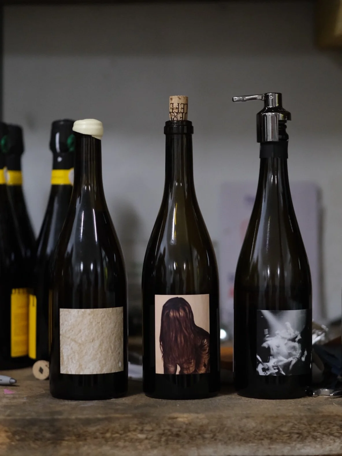 Trois bouteilles de vin avec différentes étiquettes, une avec un bouchon en liège, sur une table en bois