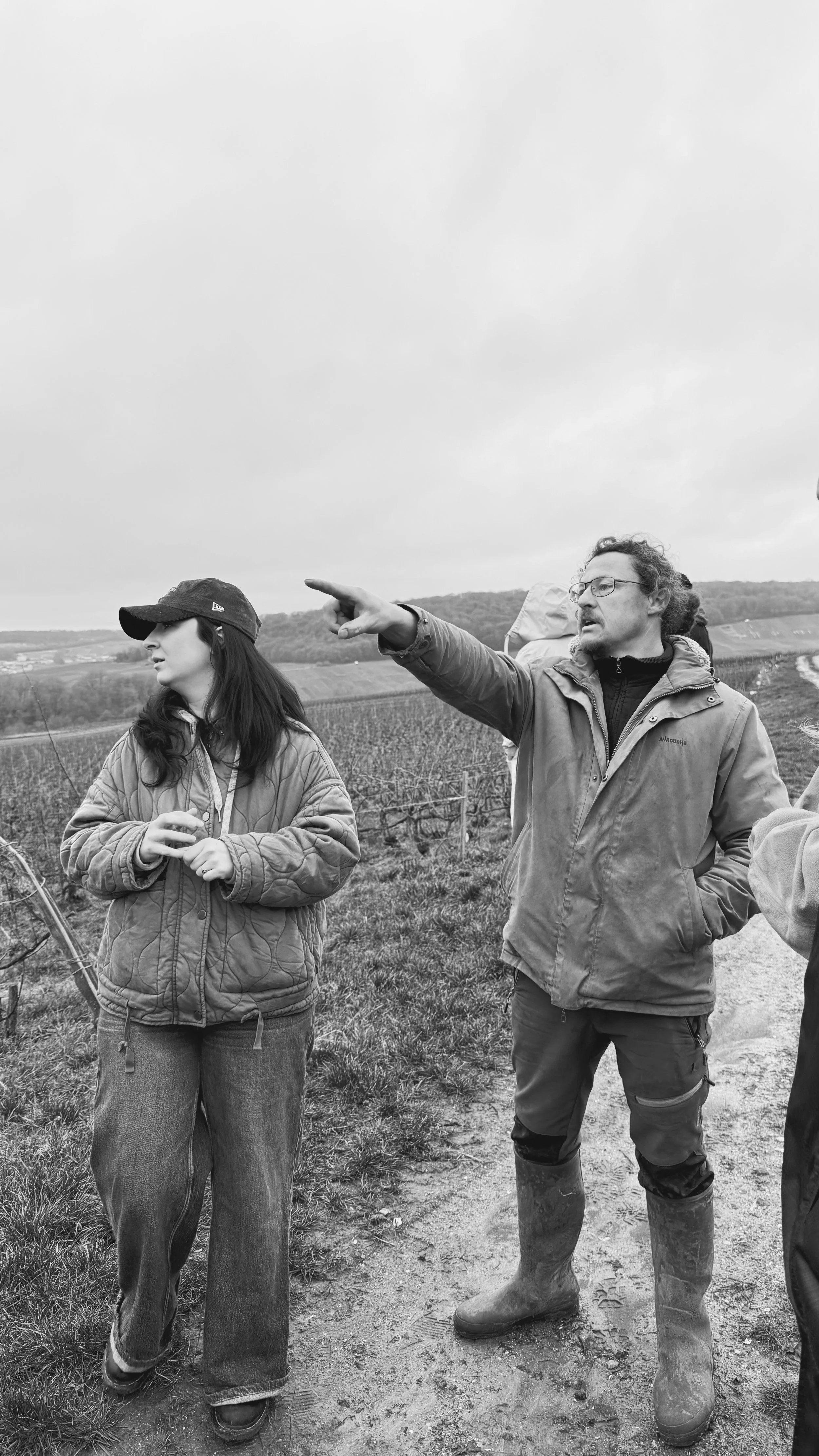 Deux personnes discutent dans un champ agricole, un homme explique quelque chose en pointant du doigt, une femme l'écoute attentivement.