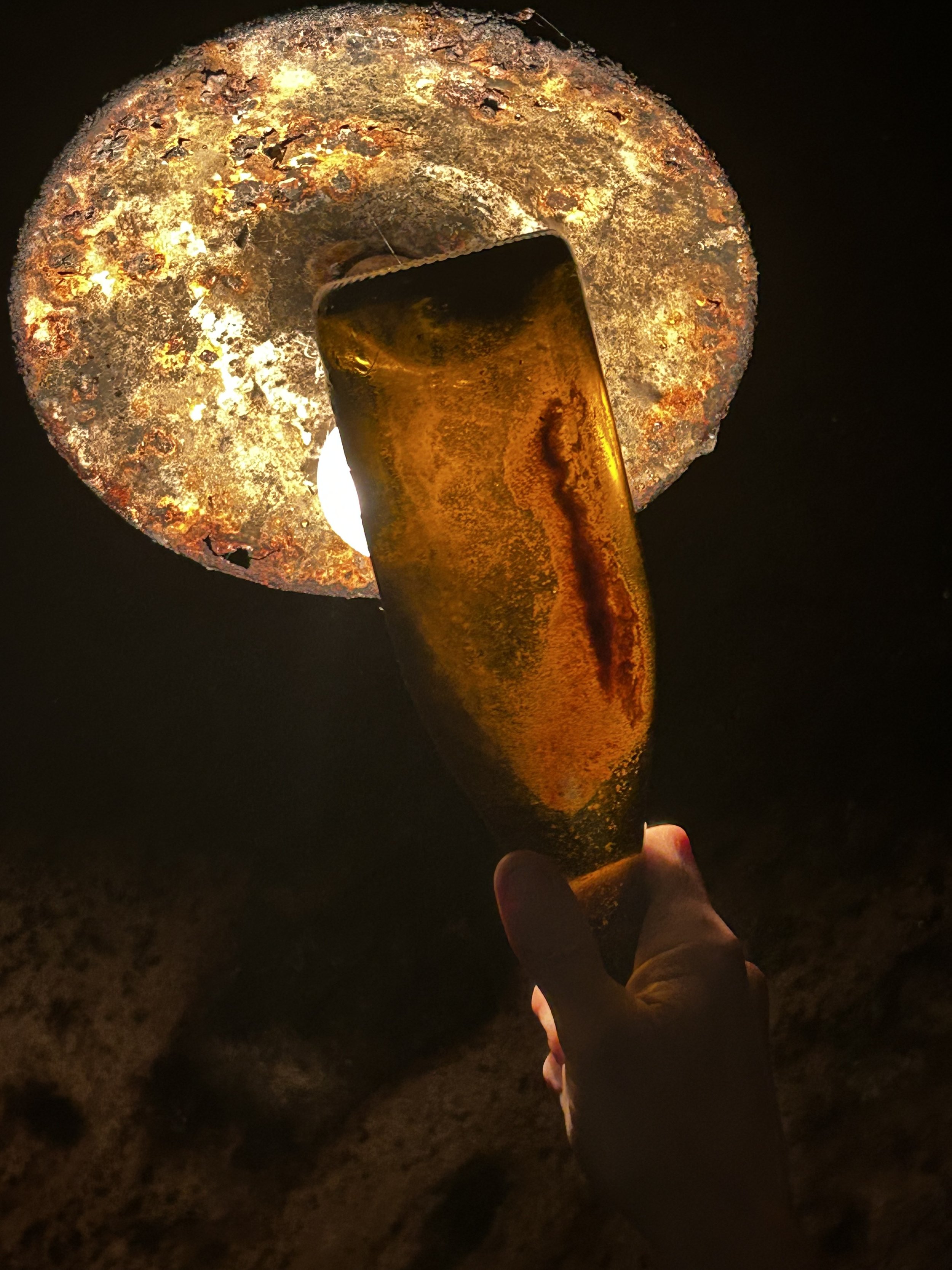 Une personne tient une lampe torche orange qui éclaire une surface sombre et une roche rouillée.