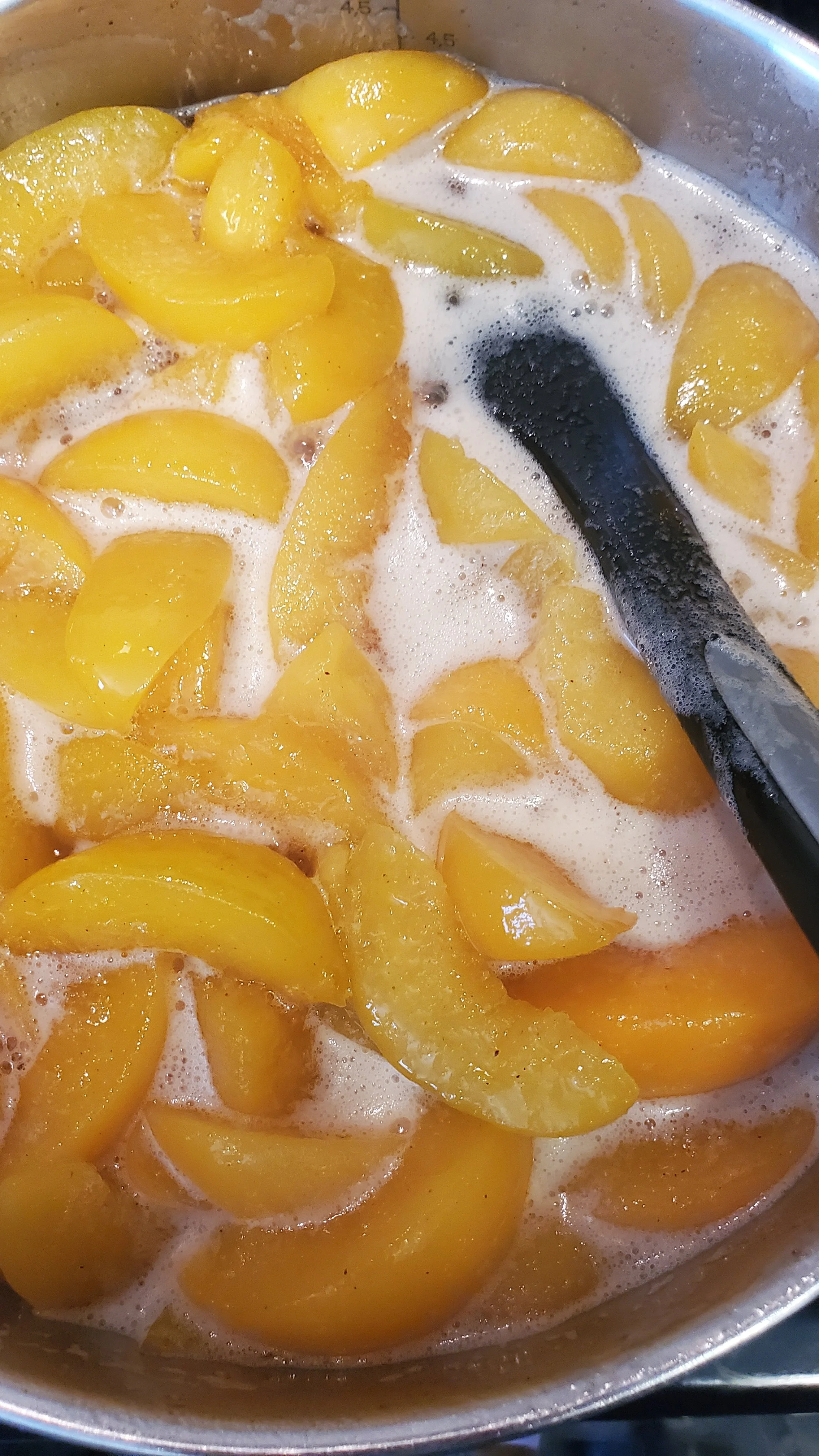 Peach slices cooking in a pot with foam and a black spoon.