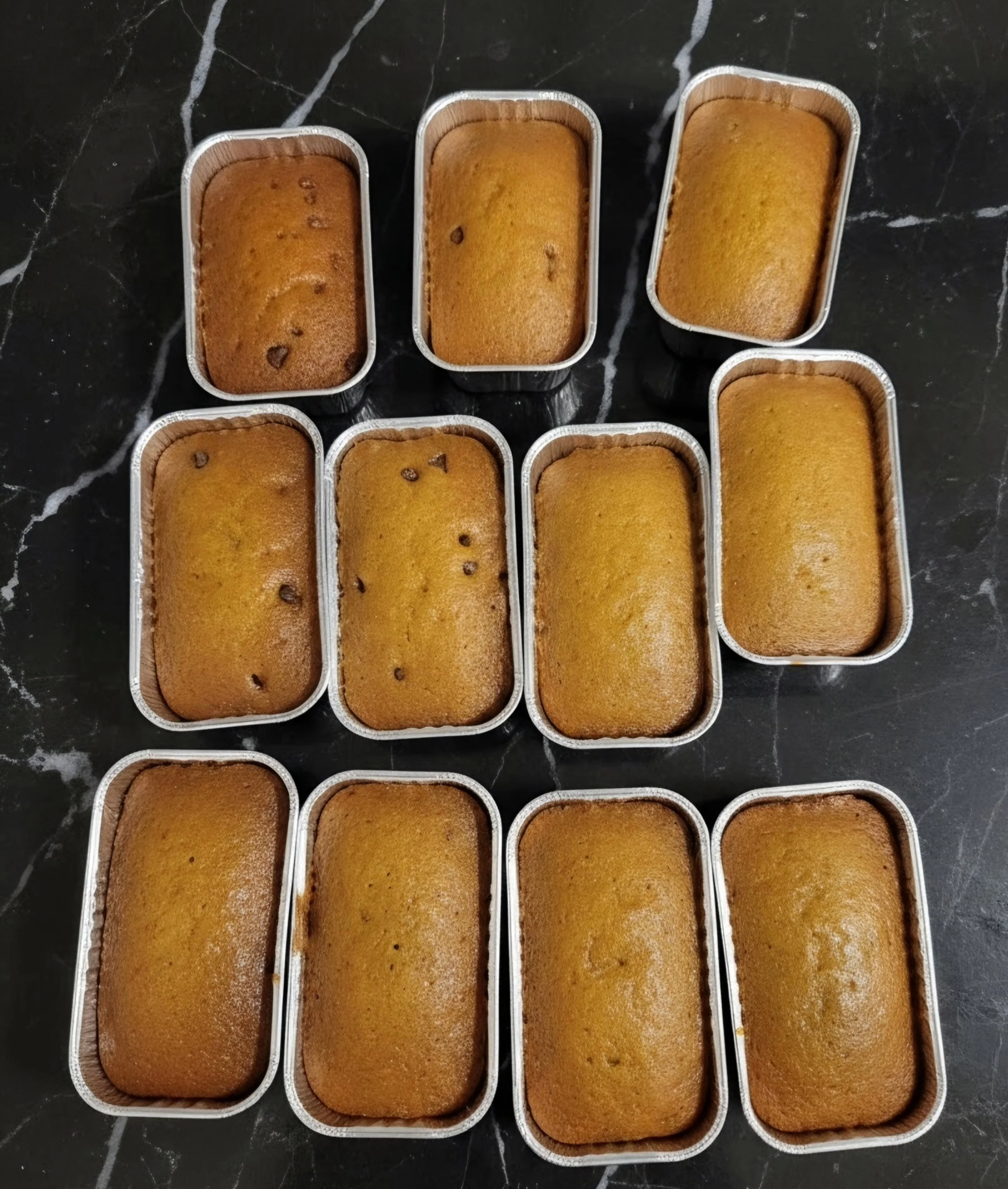 Several freshly baked loaves of bread in rectangular metal baking pans placed on a black marble countertop.