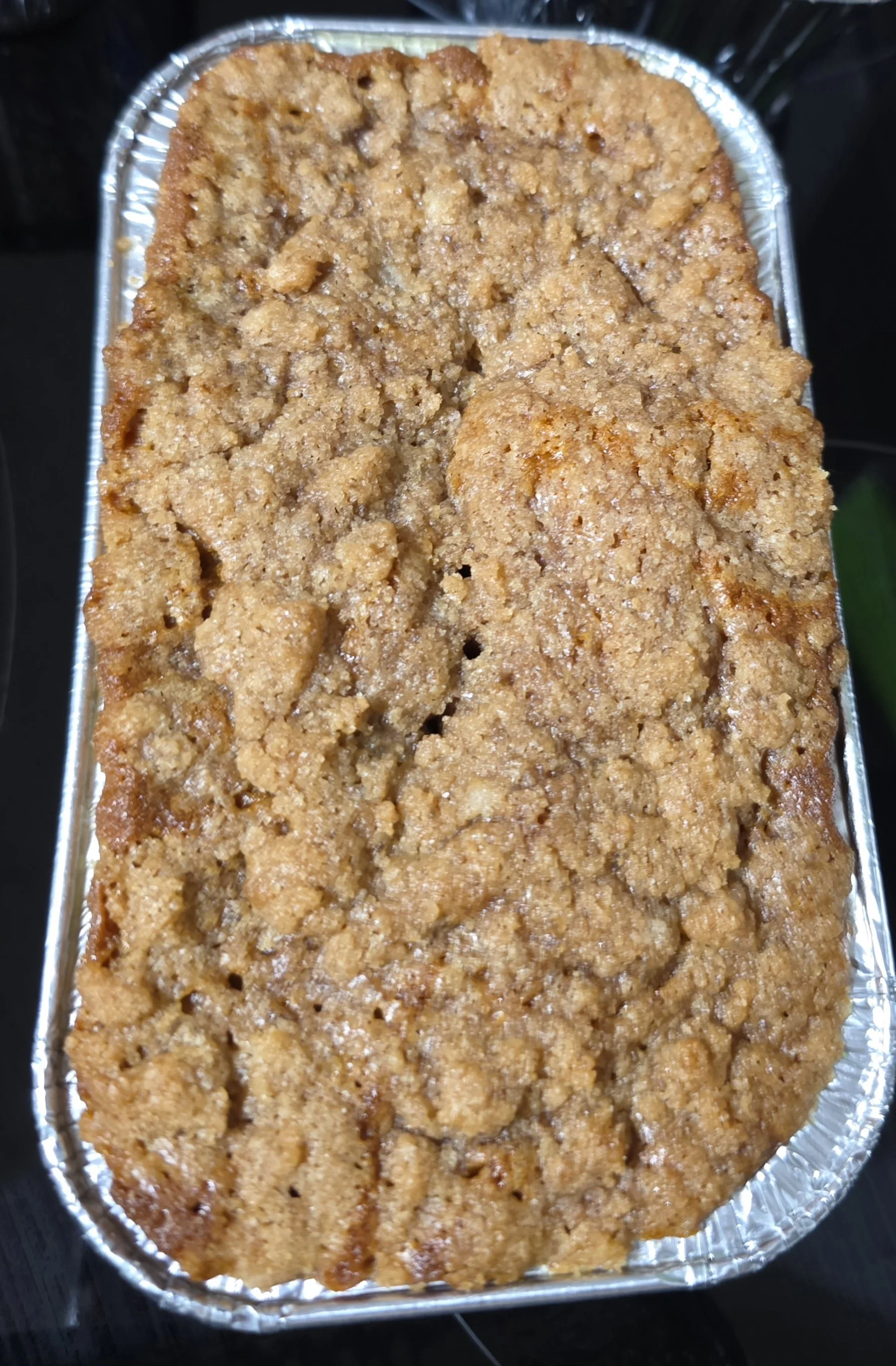 A rectangular baked dessert with a crumbly topping in a metal foil tray.