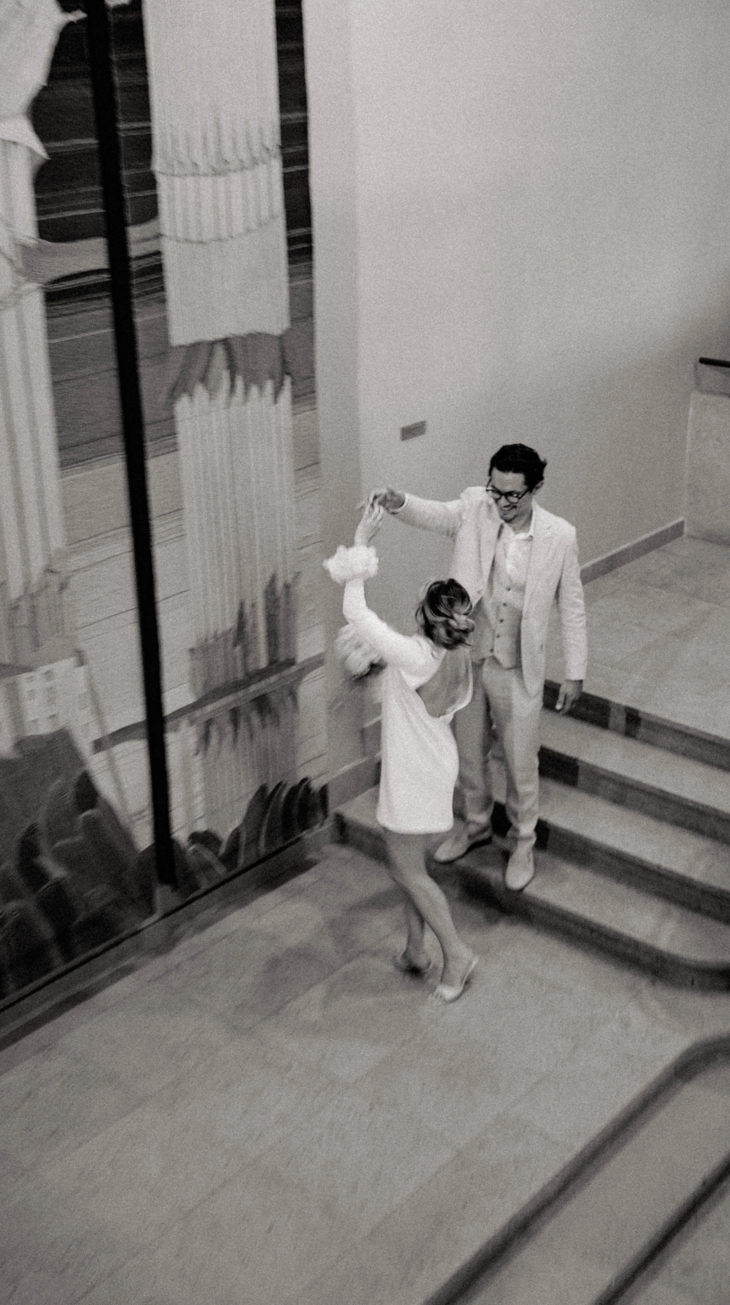 Deux personnes dansent dans une salle, une en robe blanche et l'autre en costume, lors d'une fête ou d'un événement.