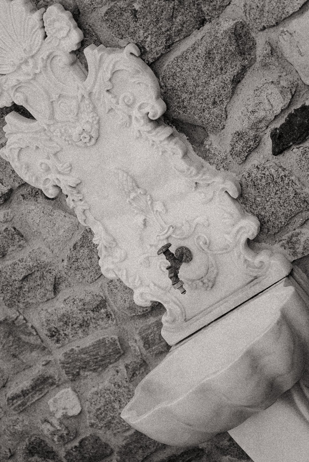 Une antique plaque en pierre sculptée ornementale fixée à un mur en briques, à côté d'une toilette en céramique avec un robinet ancien.