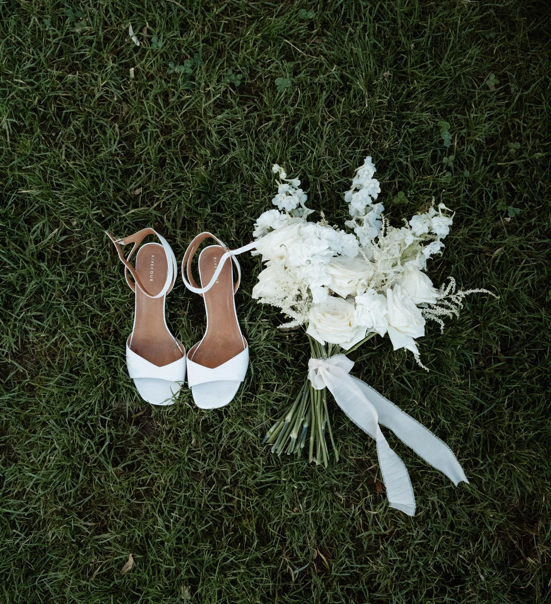 Chaussures blanches de mariage et bouquet de fleurs blanches sur de l'herbe verte
