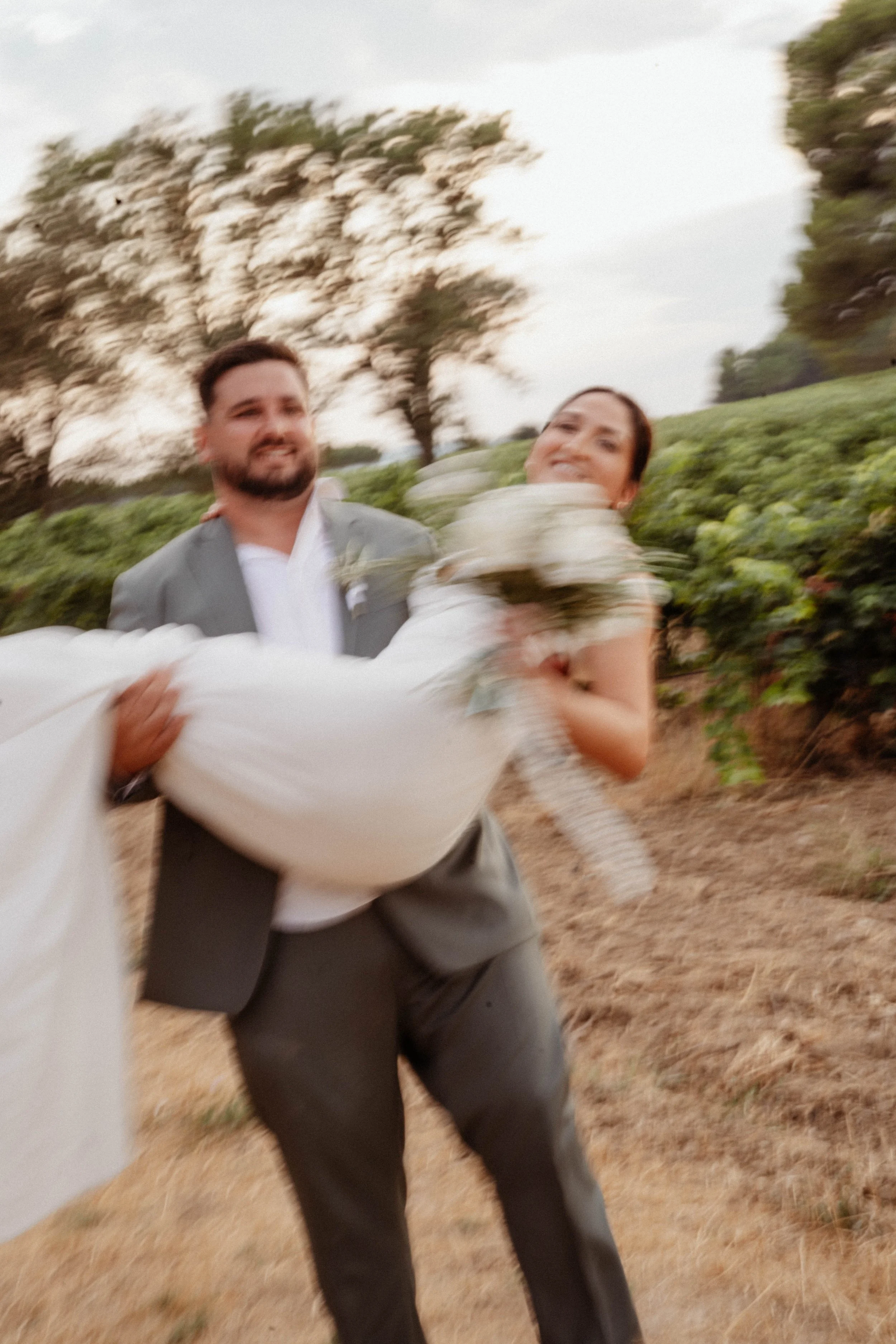 Un marié et une mariée sont en train de danser en extérieur, avec des arbres en arrière-plan, lors d'une journée ensoleillée.