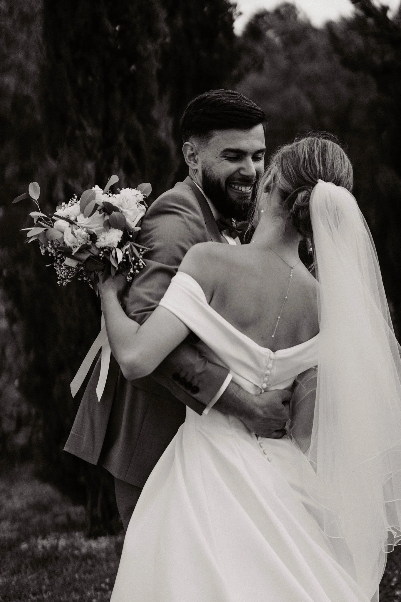 Un couple de mariés, un homme en costume et une femme en robe de mariage, s'embrassent lors d'une cérémonie de mariage en plein air.