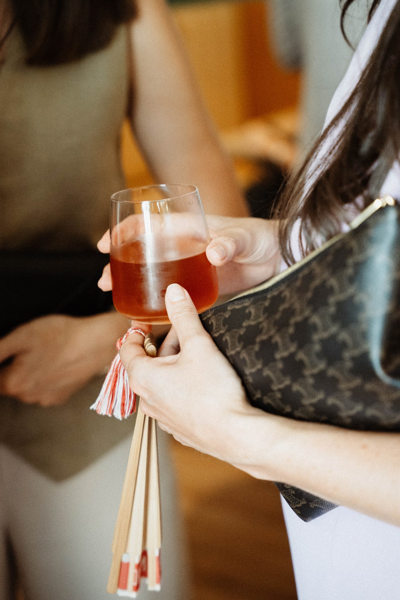 Une personne tient un verre avec une boisson rouillée, en utilisant ses doigts, avec d'autres personnes visibles en arrière-plan.