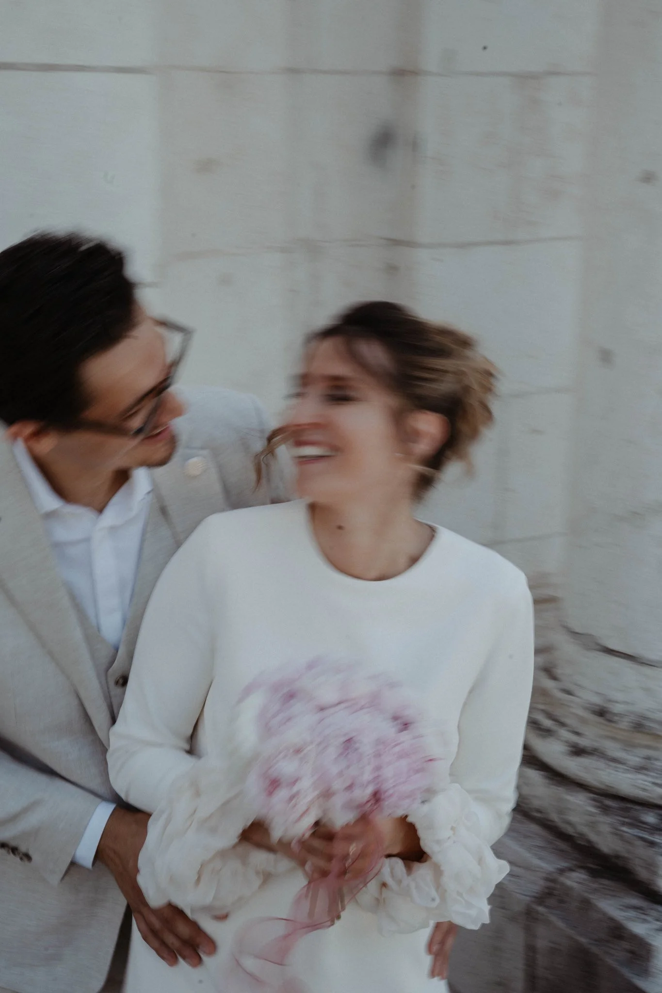 Deux personnes sourient et se regardent, portant des vêtements blancs, dans un espace lumineux avec des murs blancs.
