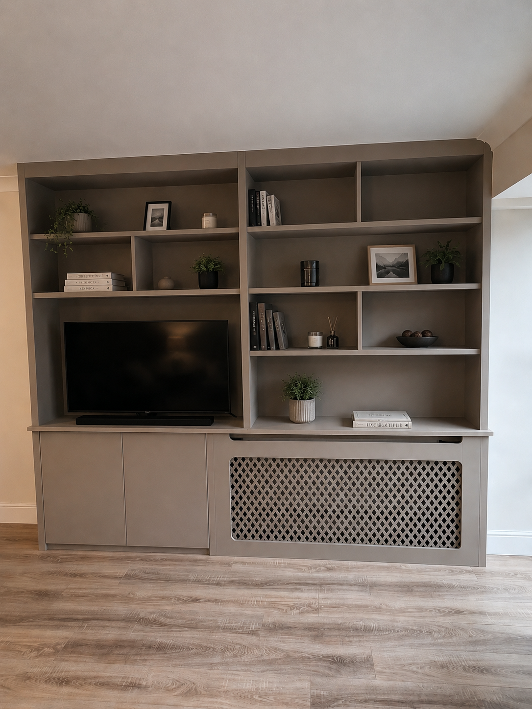 Gray shelving unit with decorative items and a TV, set against a light-colored wall on wooden flooring.