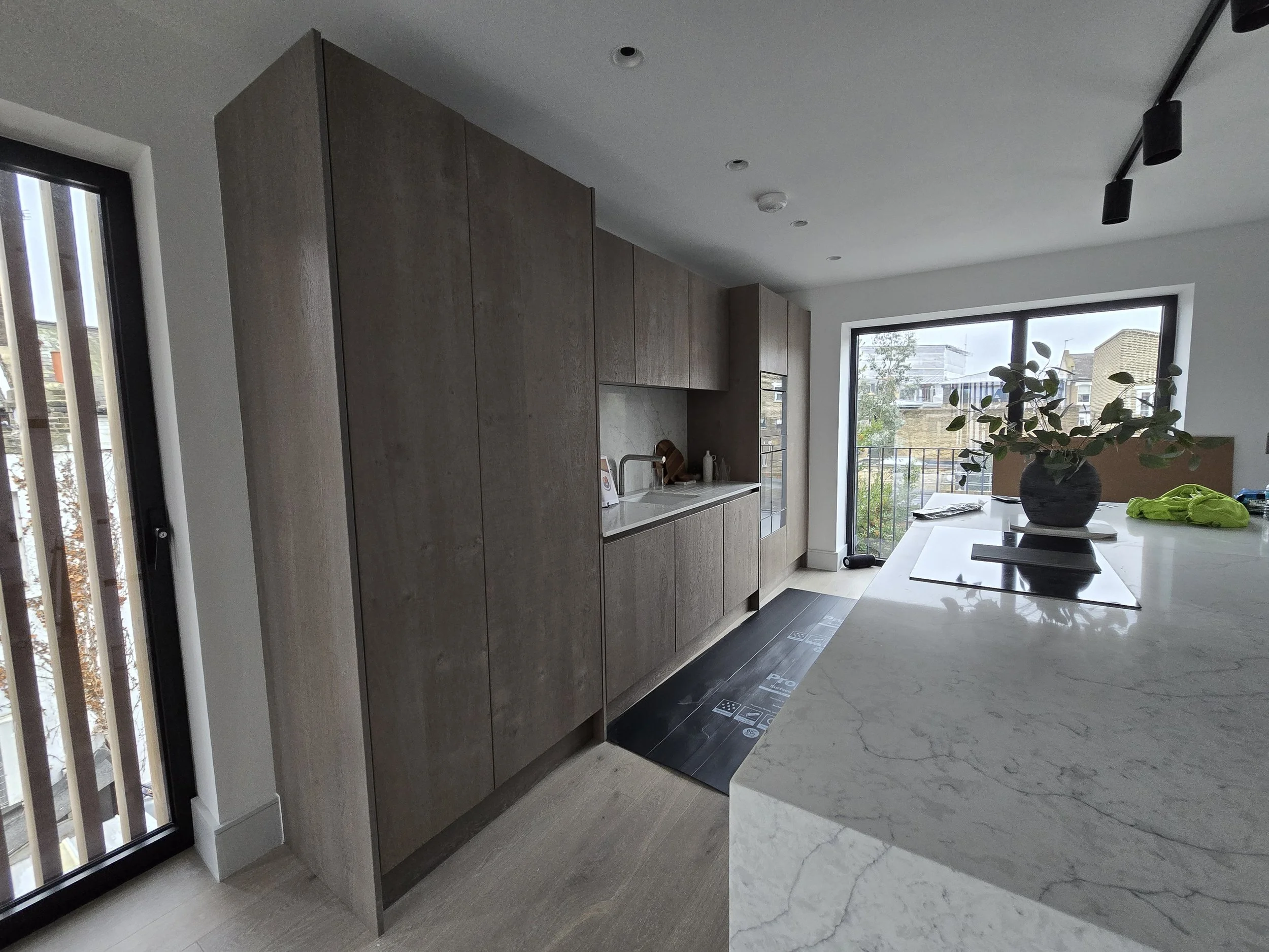 Modern kitchen with wooden cabinets, a white marble island, large windows, and potted plant.