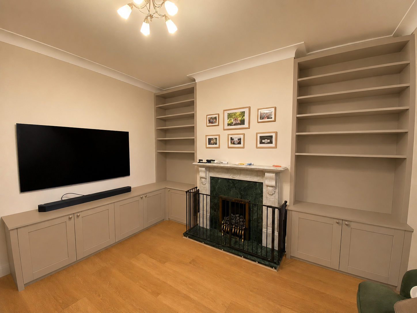 Living room with a flat-screen TV, a fireplace with a green marble surround, built-in shelves on either side, beige cabinets below, small framed pictures above the fireplace, and hardwood flooring.