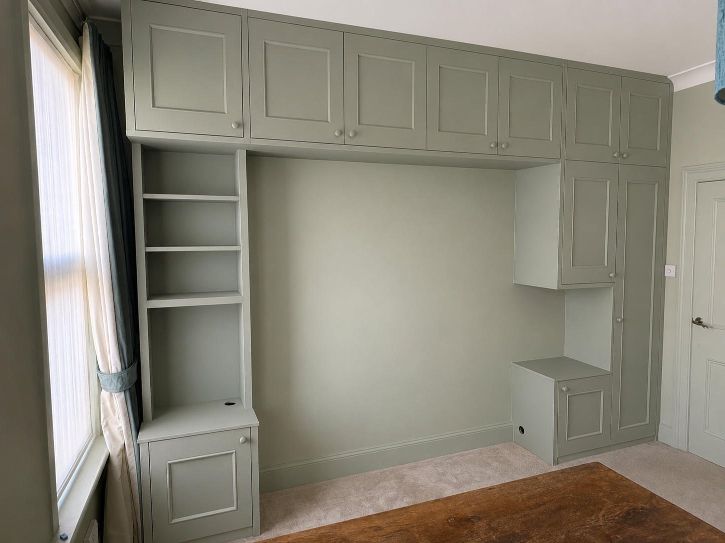 Empty built-in wall unit with cabinets, shelves, and a small closed cabinet near a window in a room.