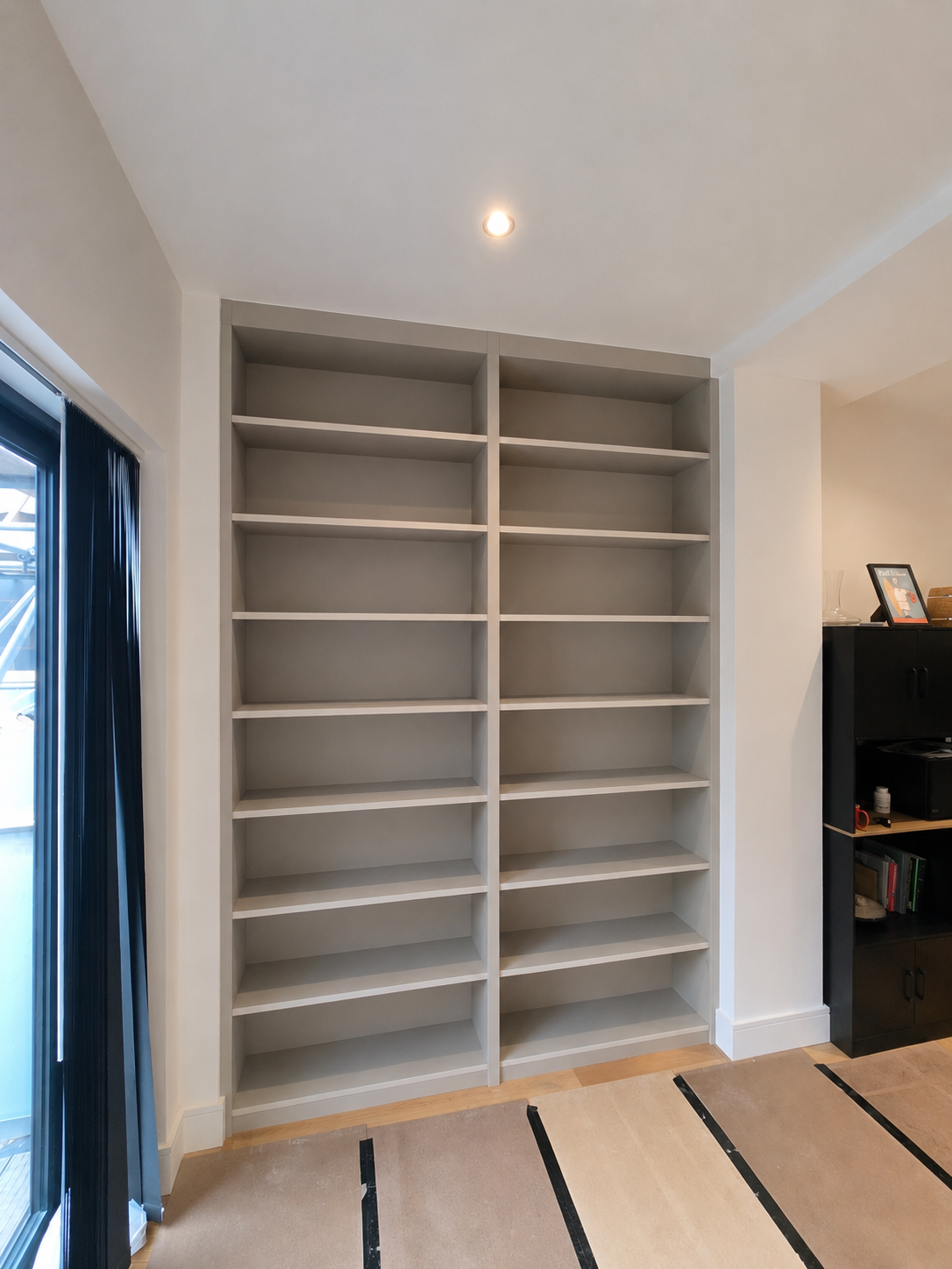 Empty white bookshelf with multiple shelves in a room with sliding glass door on the left and black cabinet on the right.