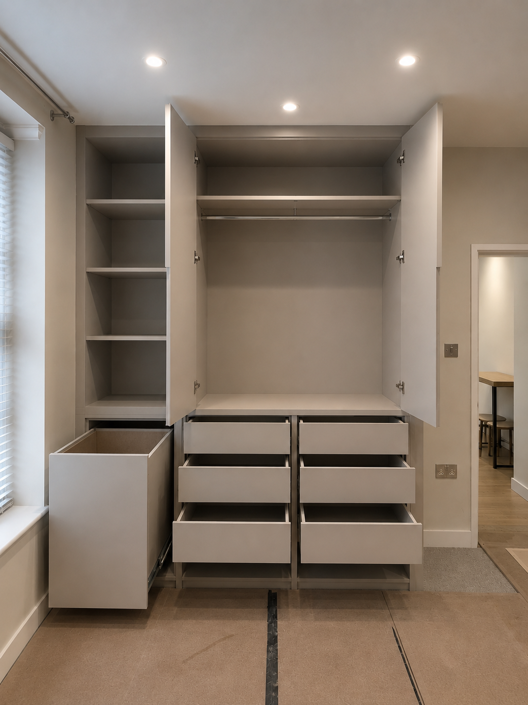 Unfinished white built-in closet with open shelves, drawers, and hanging space in a room with recessed ceiling lights.