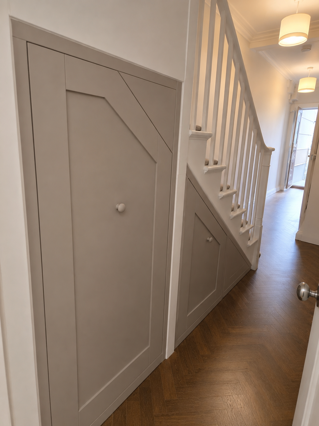 Interior view of a staircase with built-in storage cabinets underneath, featuring gray paneled doors and round white knobs.