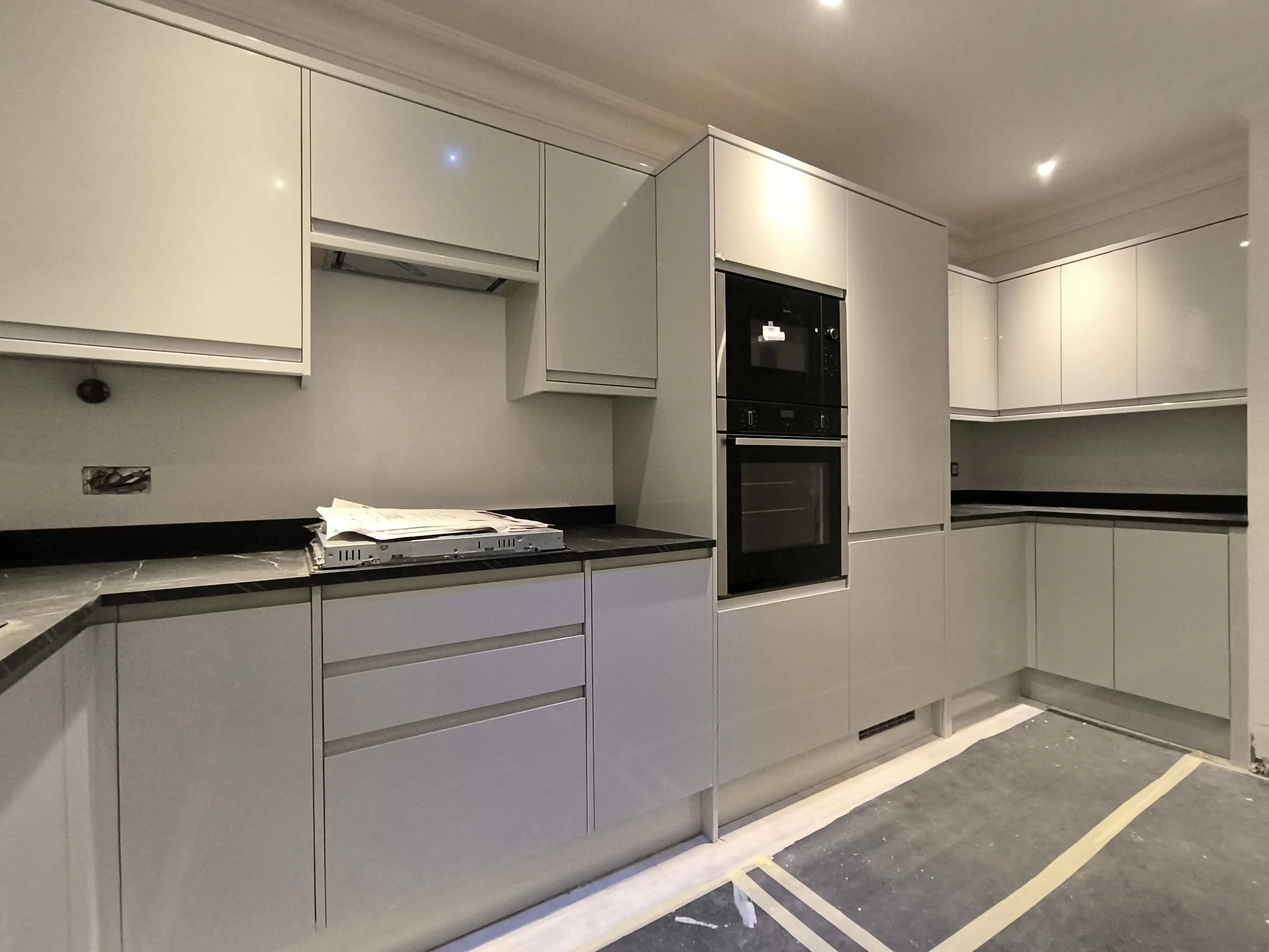 Partially installed kitchen cabinets with some open and closed sections, a built-in oven, and a countertop with construction materials and tools on it, indicating ongoing kitchen renovation.