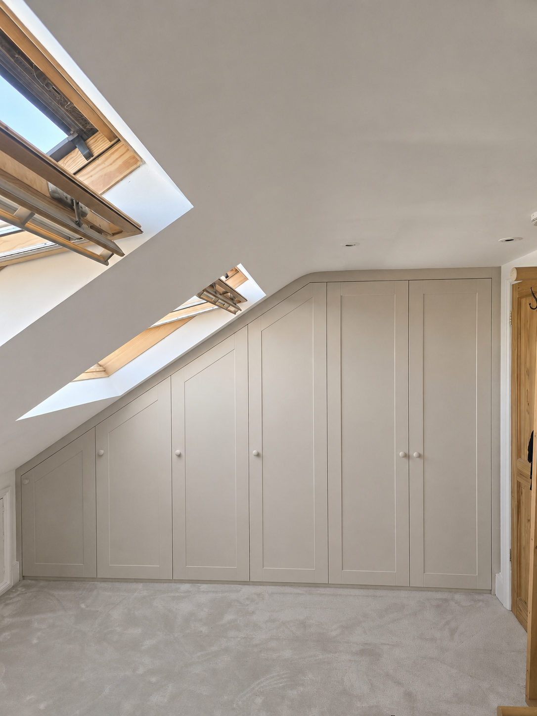 Room with sloped ceiling and built-in beige storage cabinets, three skylight windows, and light-colored carpeted floor.