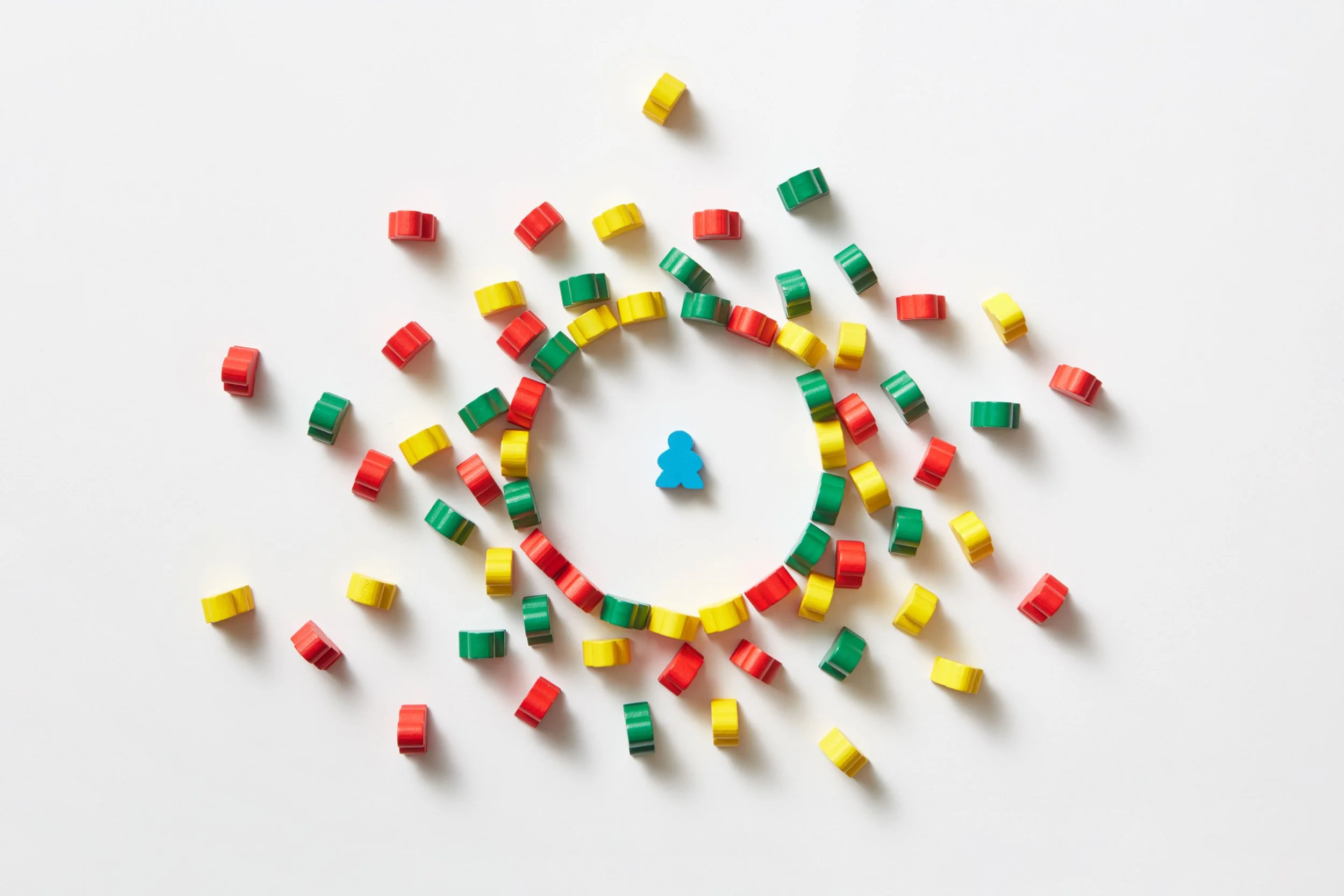 Colorful plastic game pieces and a small blue game token on a white surface, arranged in a scattered pattern.