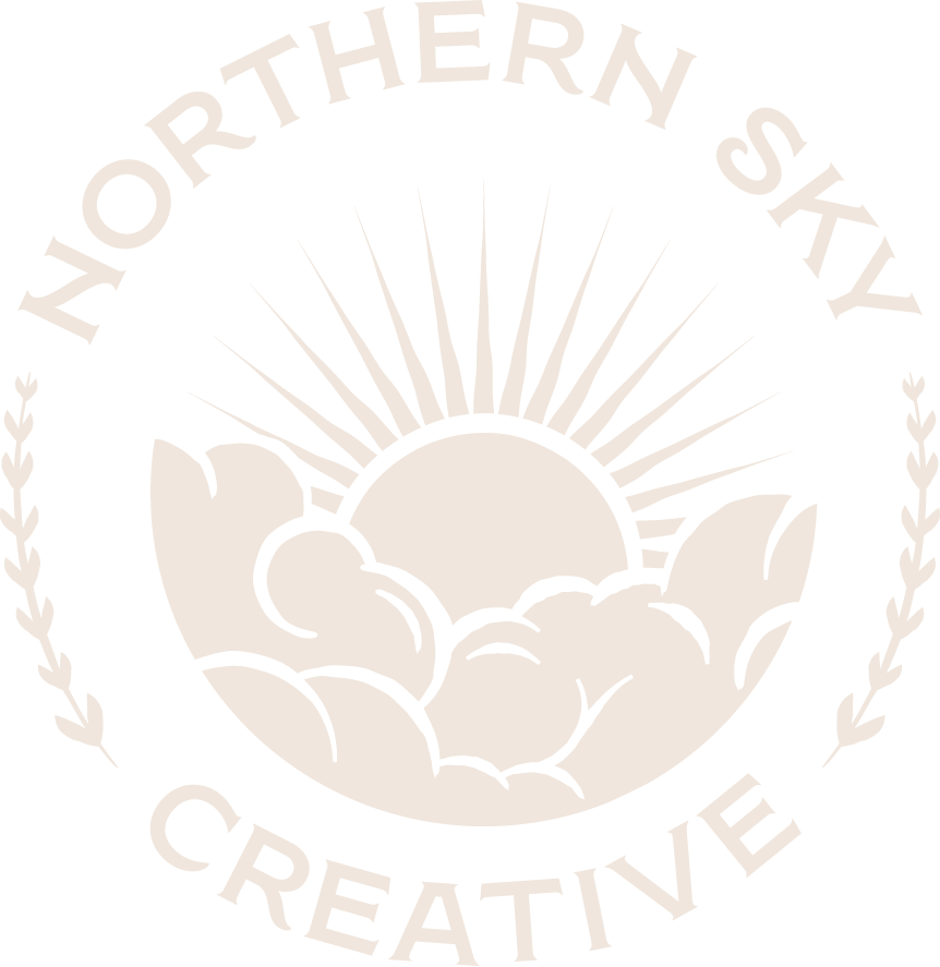Logo of Northern Sky Creative featuring a sun rising over clouds, with branches on either side.