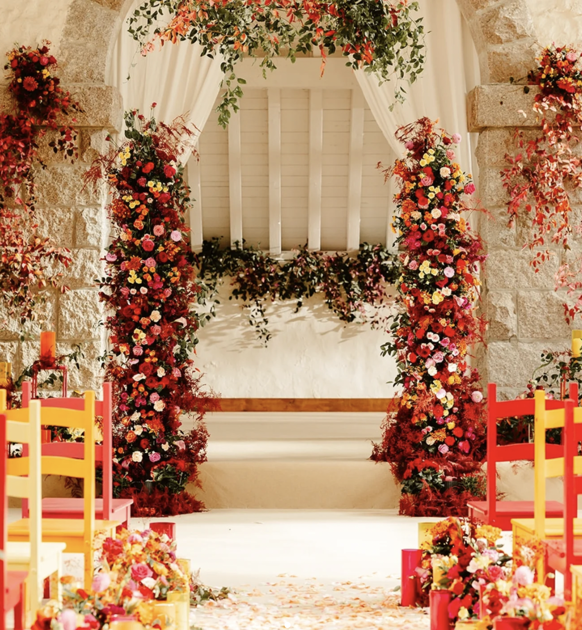 A decorated wedding aisle with a floral arch and colorful chairs.