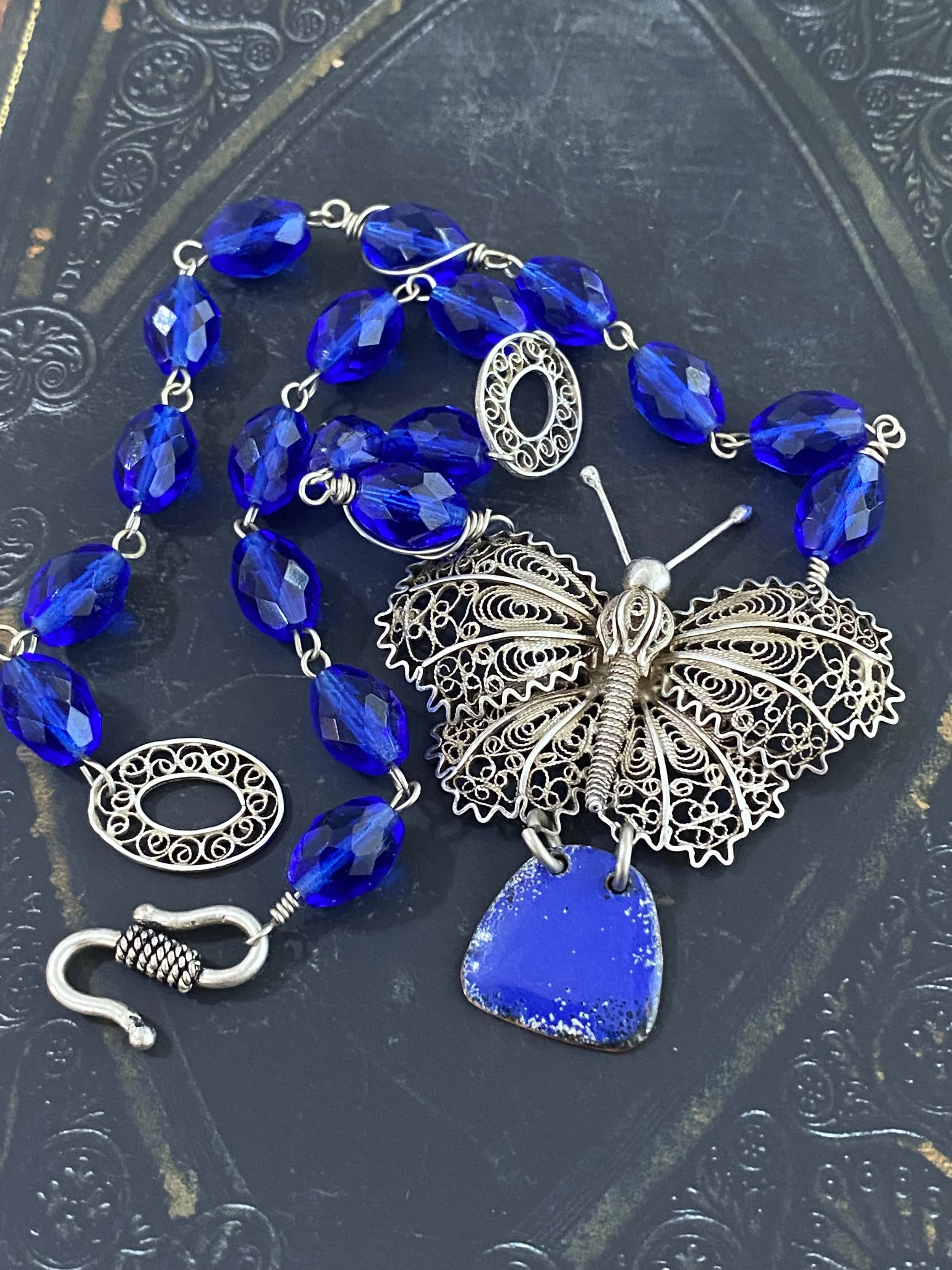 A piece of jewelry with blue beads and a silver butterfly pendant on a dark textured background.
