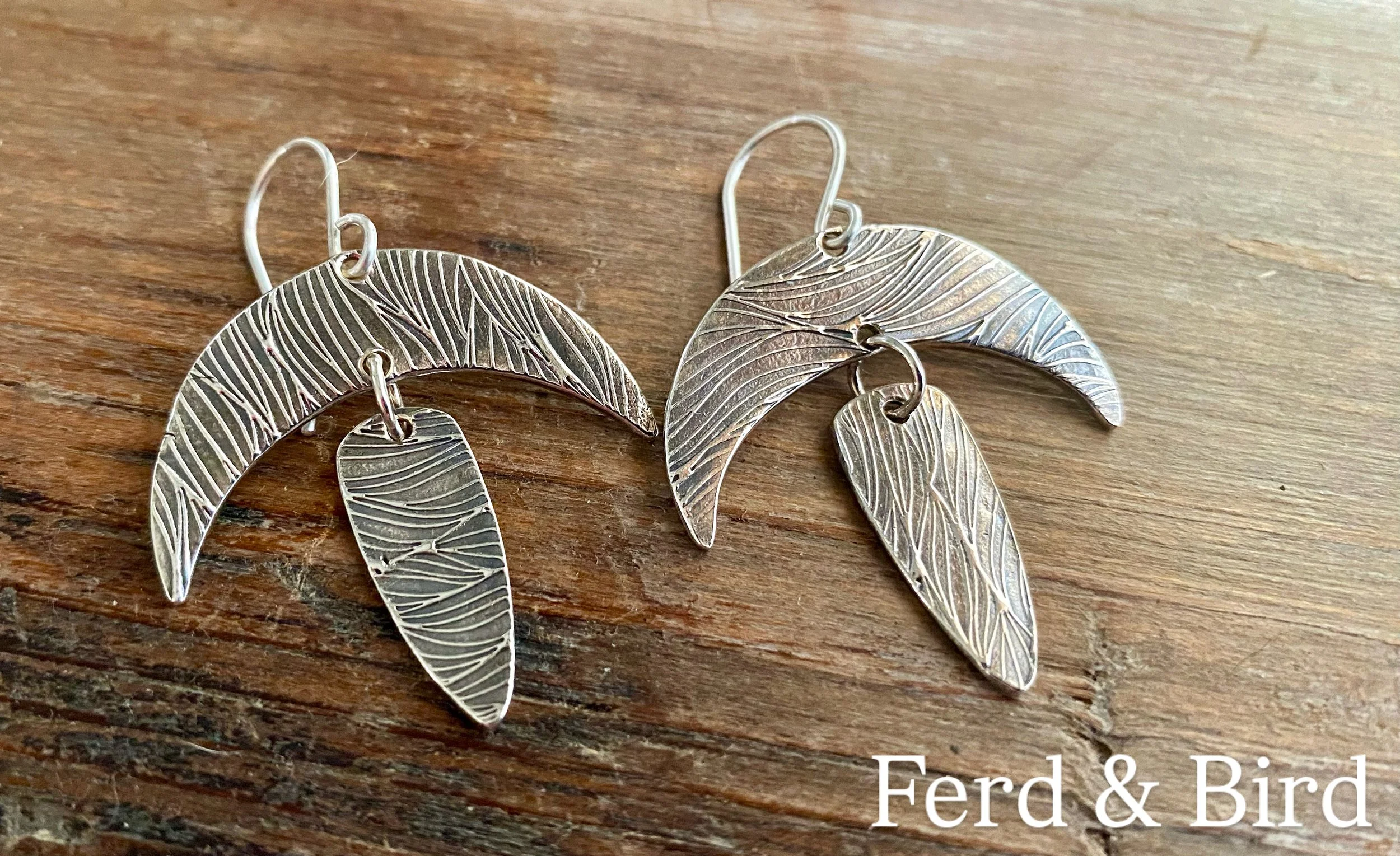 Silver earrings with feather design placed on a wooden surface.