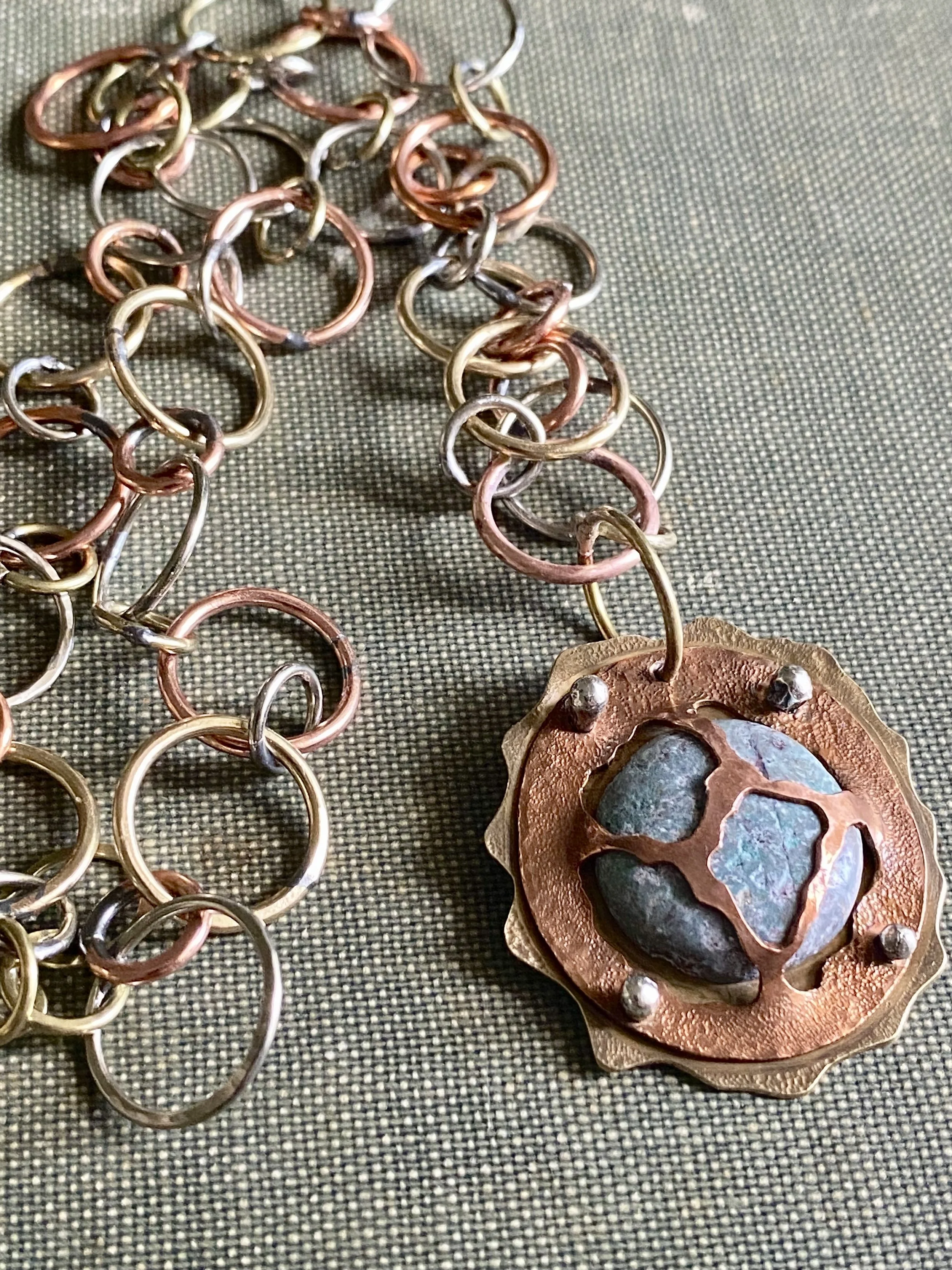 Close-up of tangled colorful metal rings and a decorative piece with stones on a textured surface.