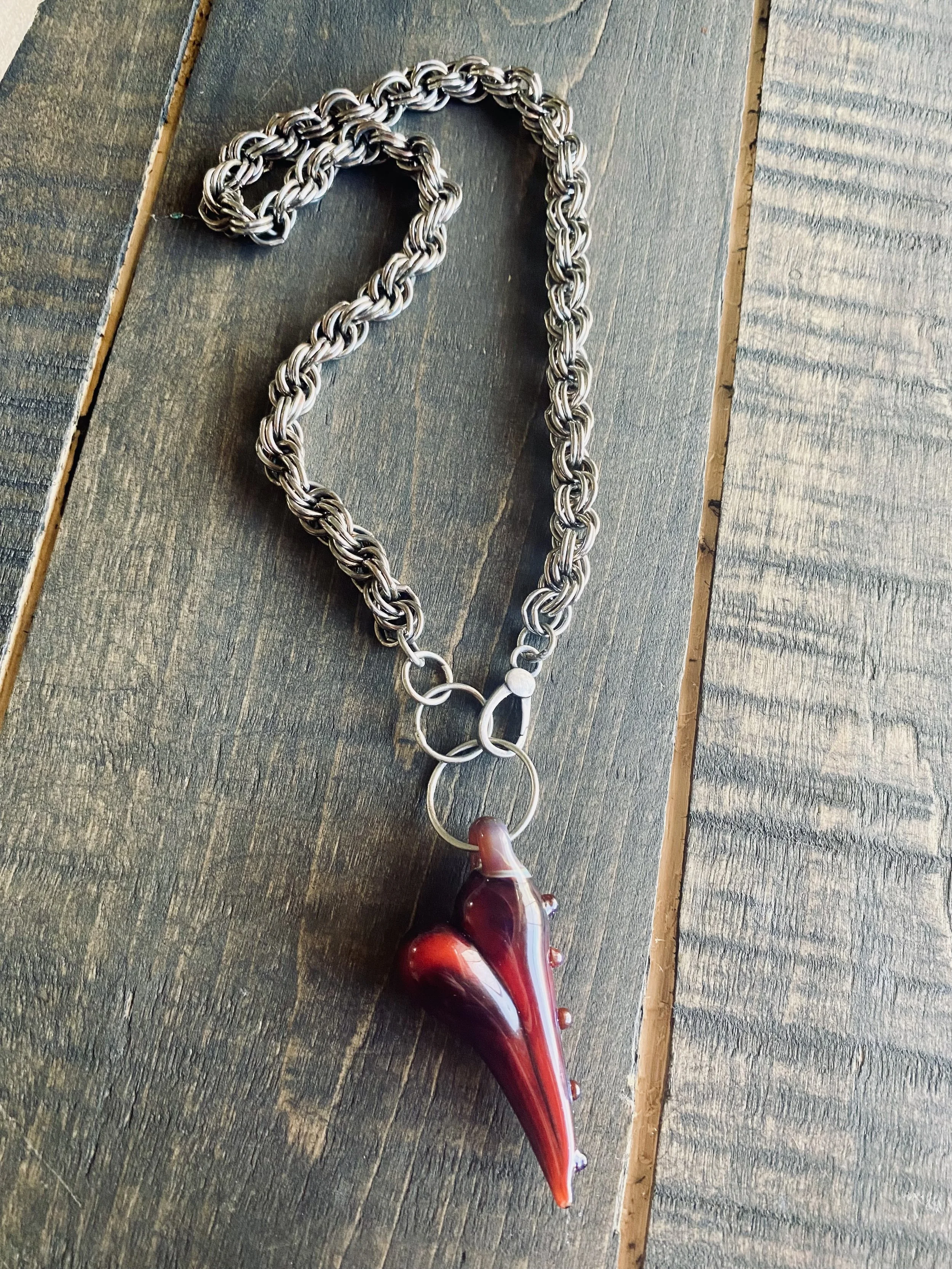 A silver chain necklace with a large shell pendant featuring a red and white swirl pattern, lying on a wooden surface.