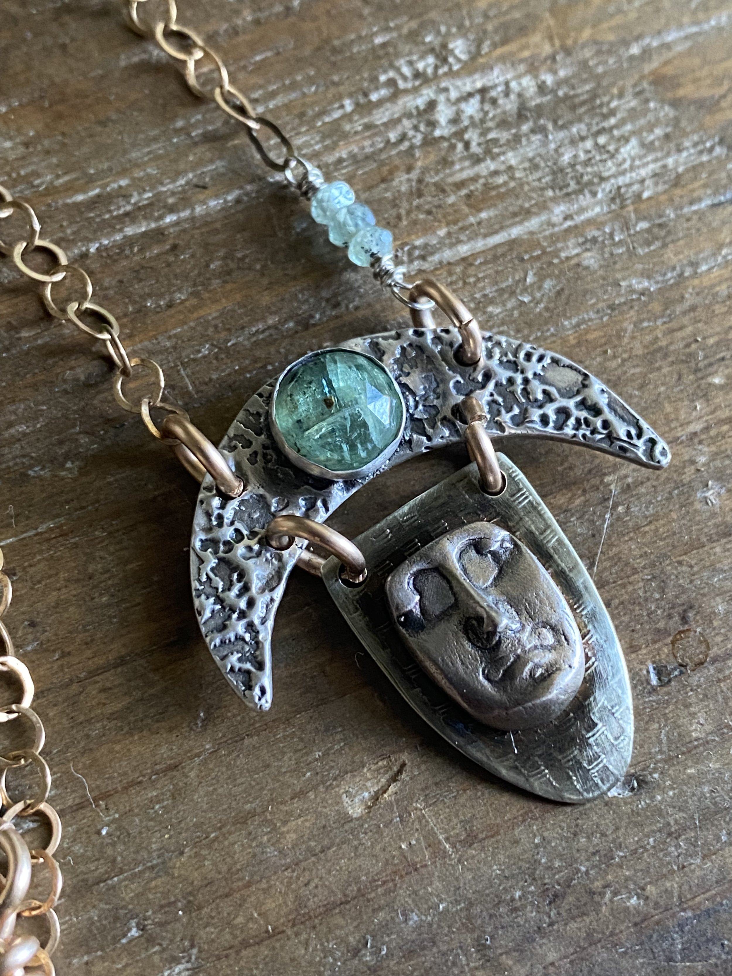 Close-up of a silver and gold necklace with a large silver crescent-shaped pendant hanging from a chain of gold links, lying on a wooden surface.