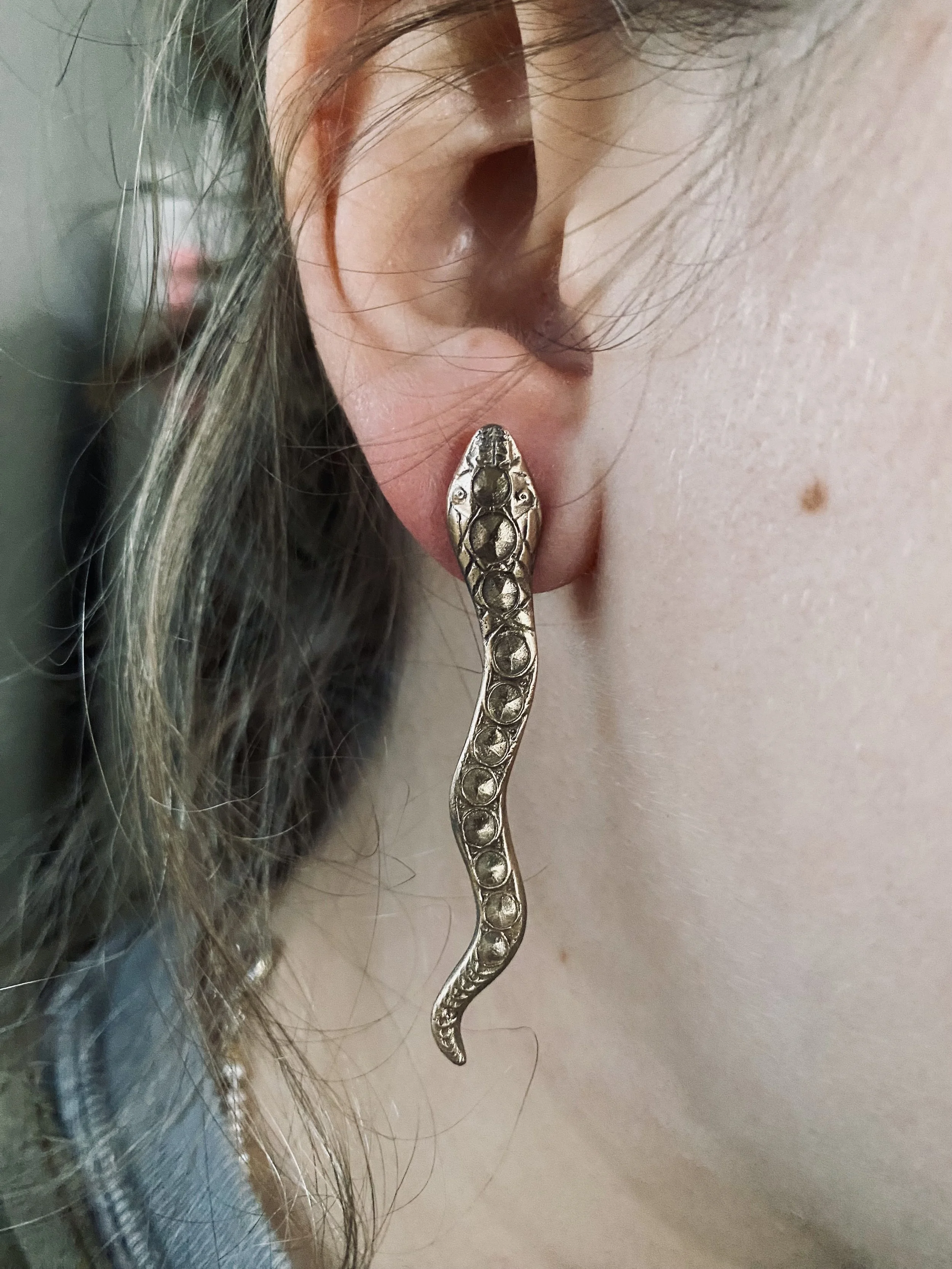 Close-up of a person's ear with a decorative snake-shaped earring.