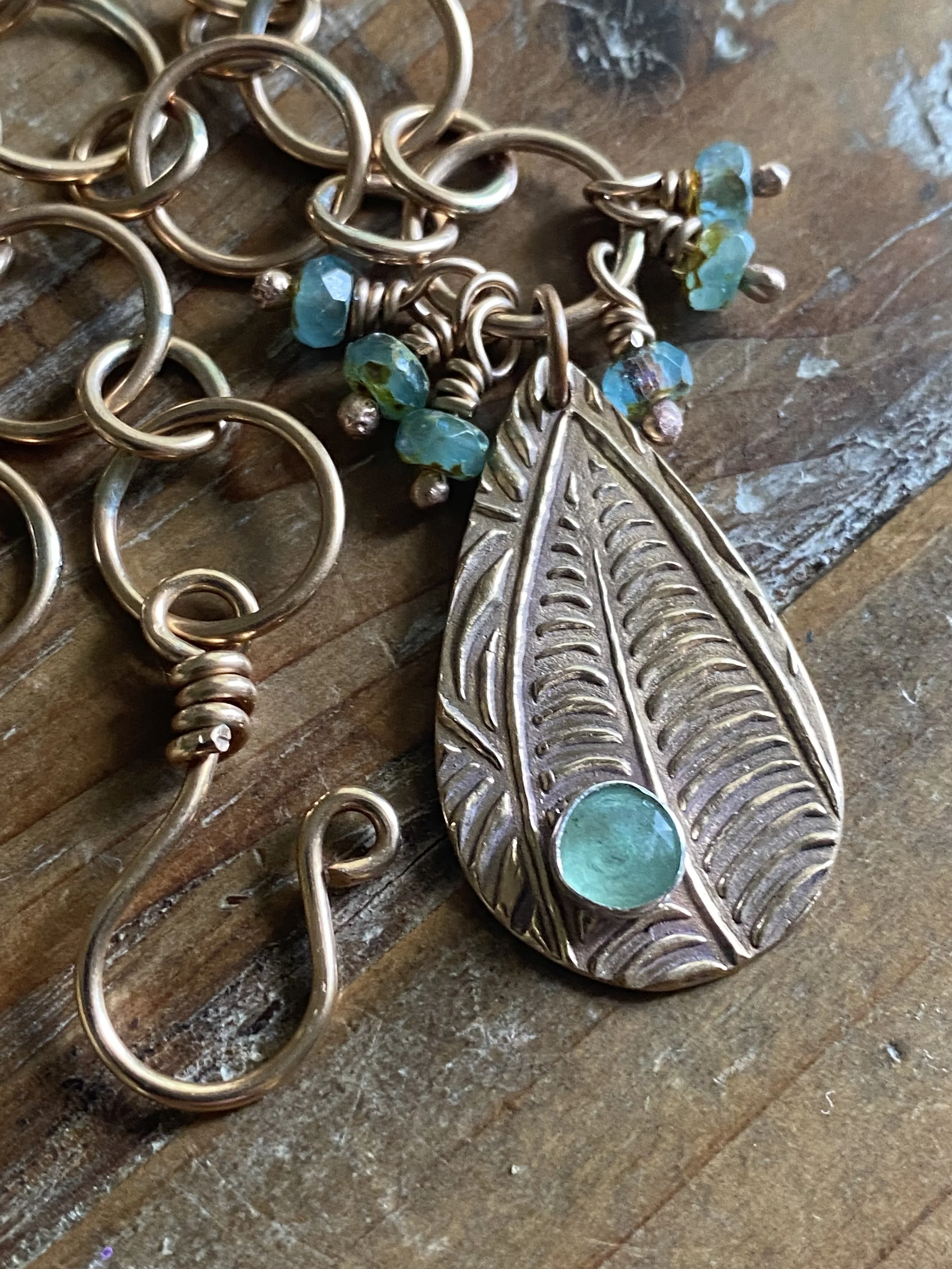 A silver metal bracelet with dangling decorative charms including a leaf-shaped charm and blue beads, lying on a wooden surface.