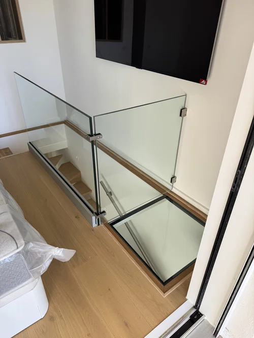 Garde-corps en verre feuilleté avec pinces inox et main courante bois sur une trémie d’escalier