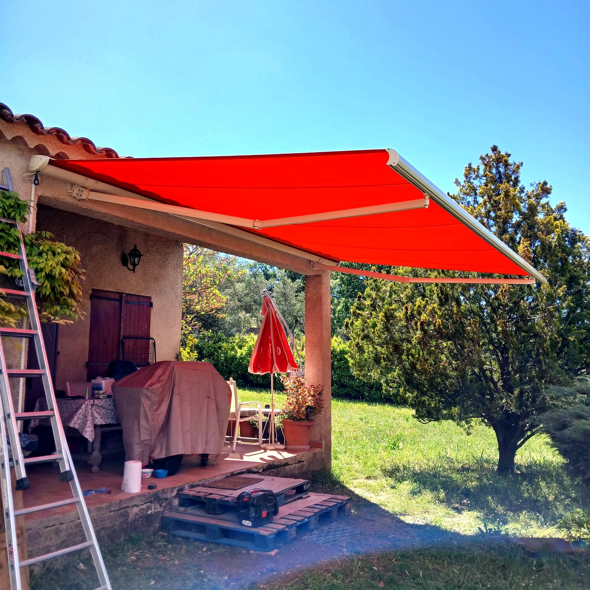 Store banne rouge déployé au-dessus de la terrasse d’une maison provençale