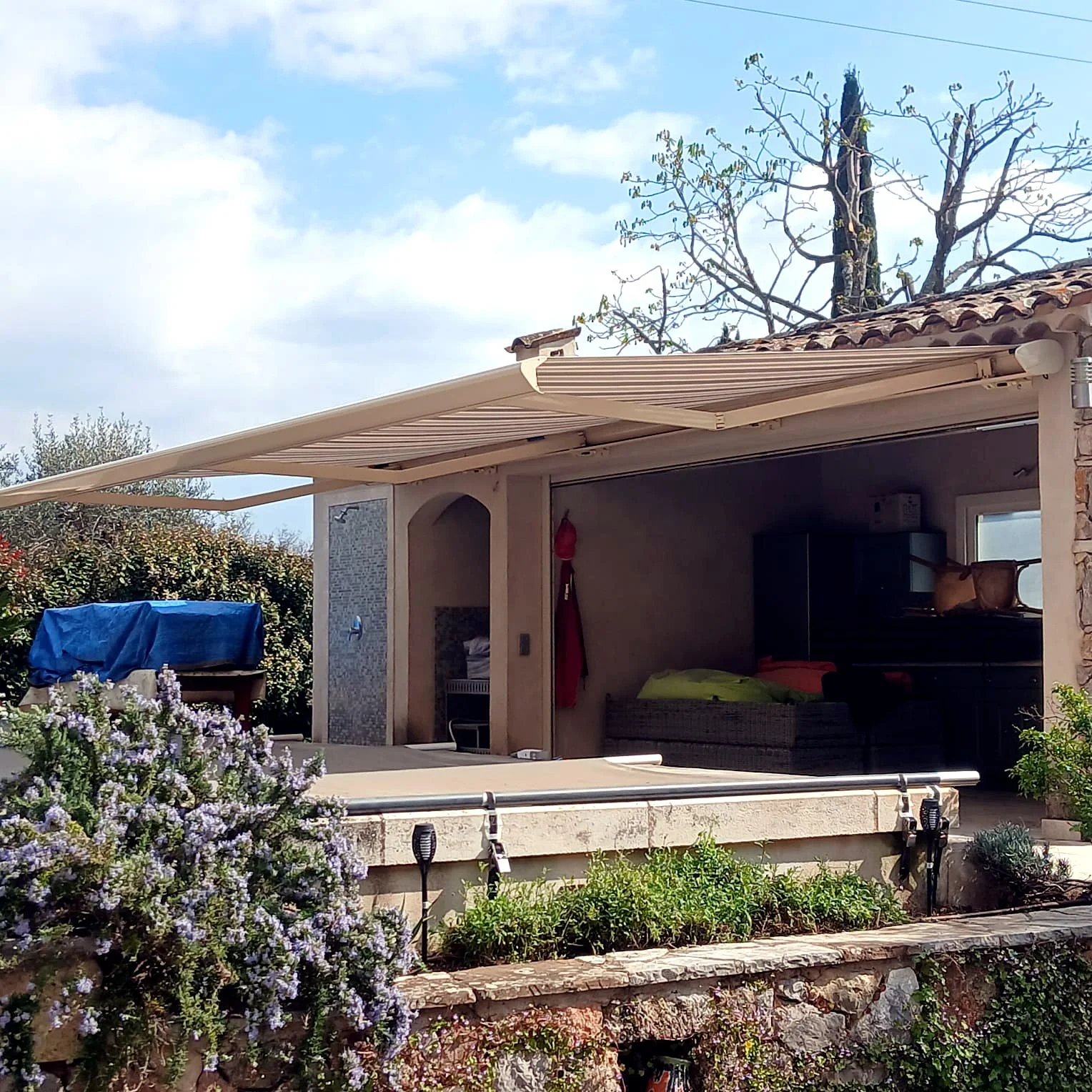 Store banne écru déployé au-dessus d’une terrasse couverte, vu de côté