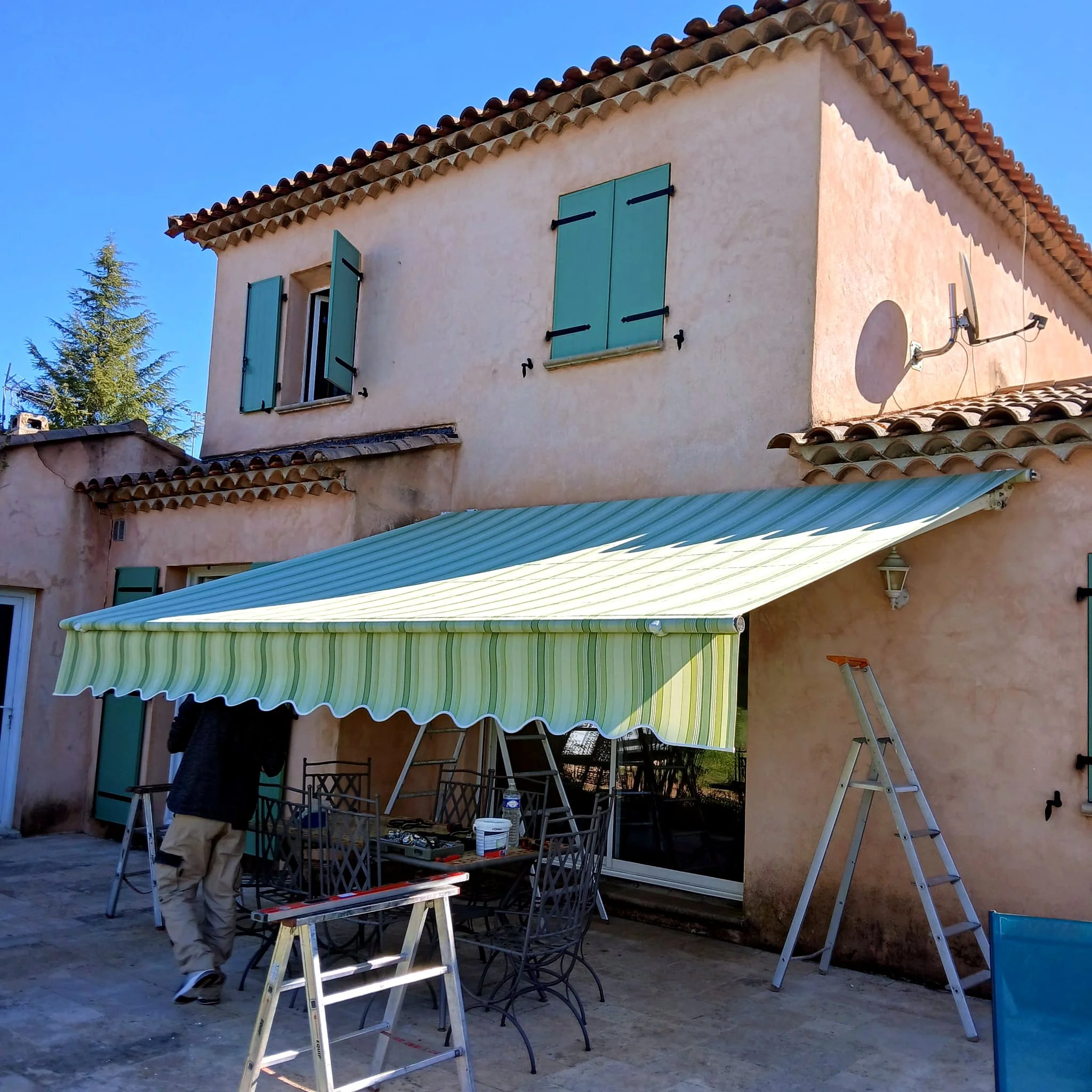 Store banne à rayures vertes et blanches sur une maison provençale à volets vert d’eau